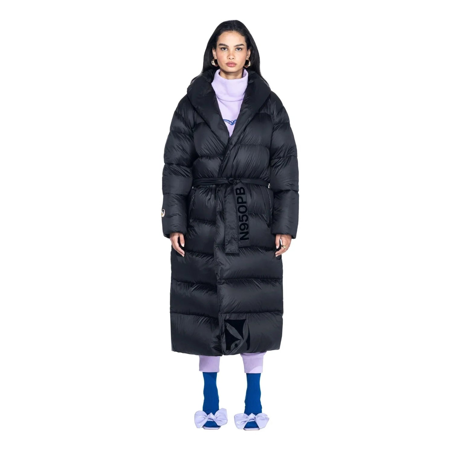 Woman wearing long black belted puffer jacket, purple pants, and blue bow slippers