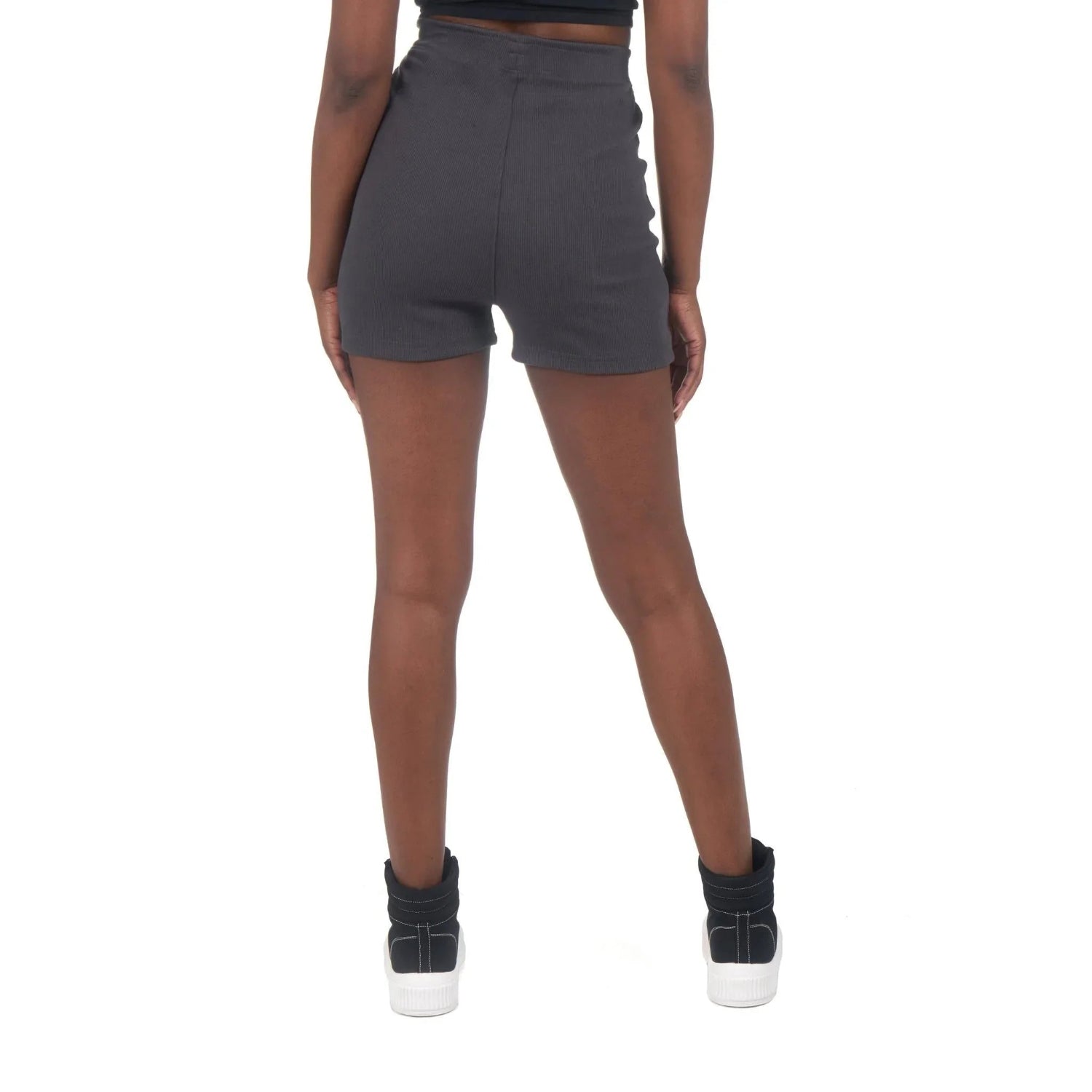 Woman wearing high-waisted black biking shorts and sneakers, rear view, on white background