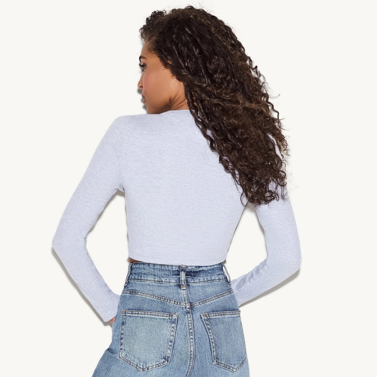 Woman wearing light blue long sleeve cropped cardigan and high-waisted denim jeans, back view