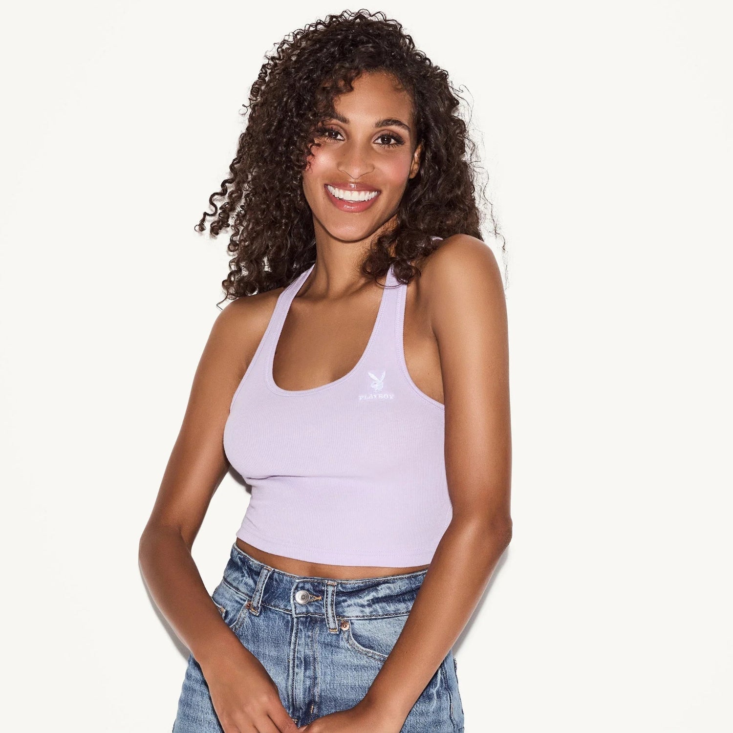 Woman wearing lilac racerback tank top with white logo and blue denim jeans