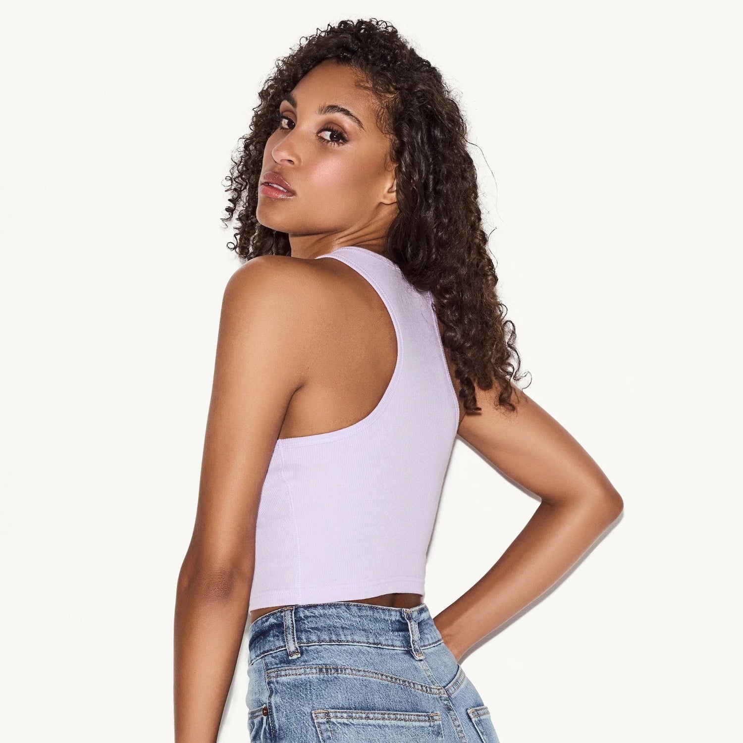 Woman in a light purple racerback tank top and blue denim jeans, back view.