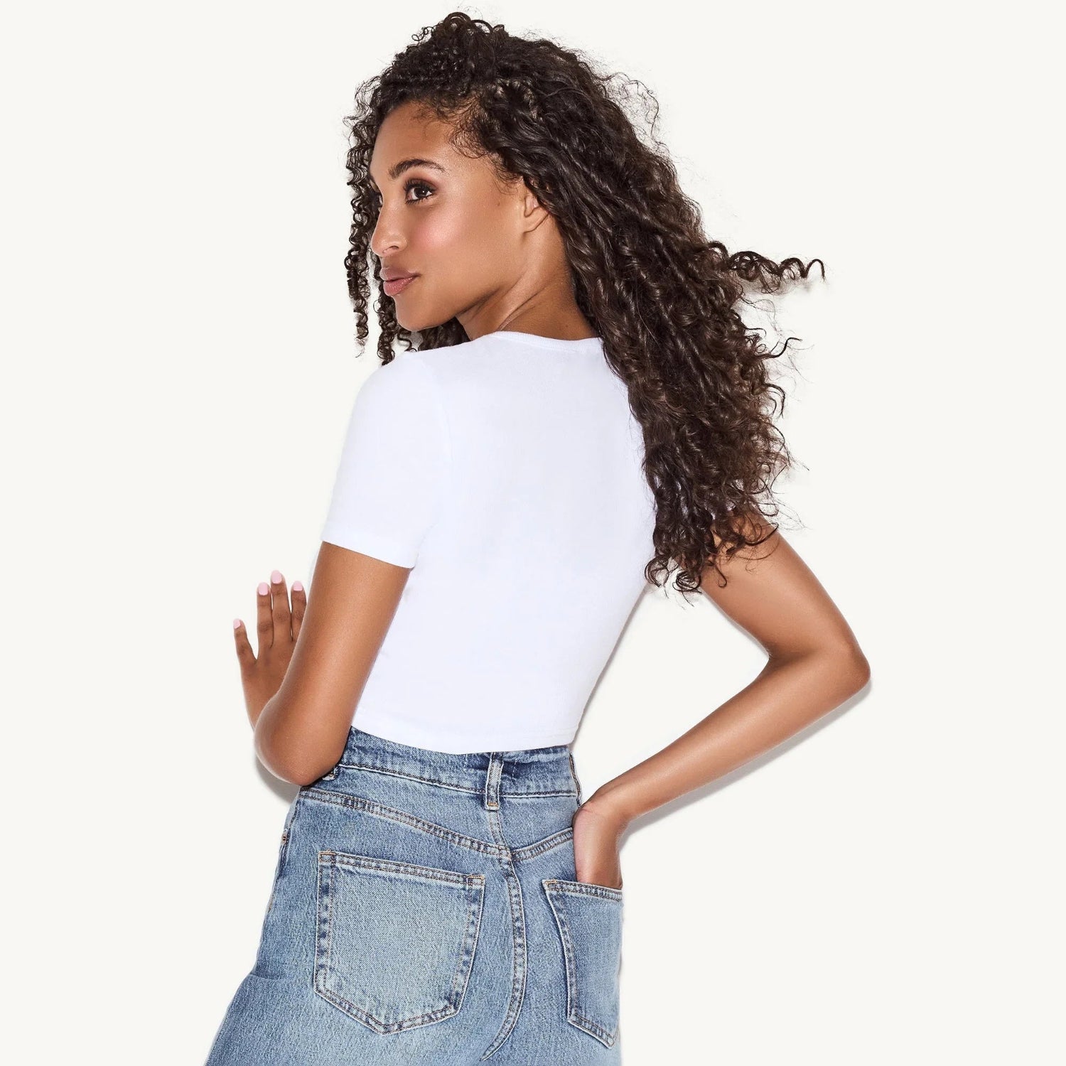 Woman wearing a fitted white baby tee and high-waisted blue denim jeans, shown from the back.