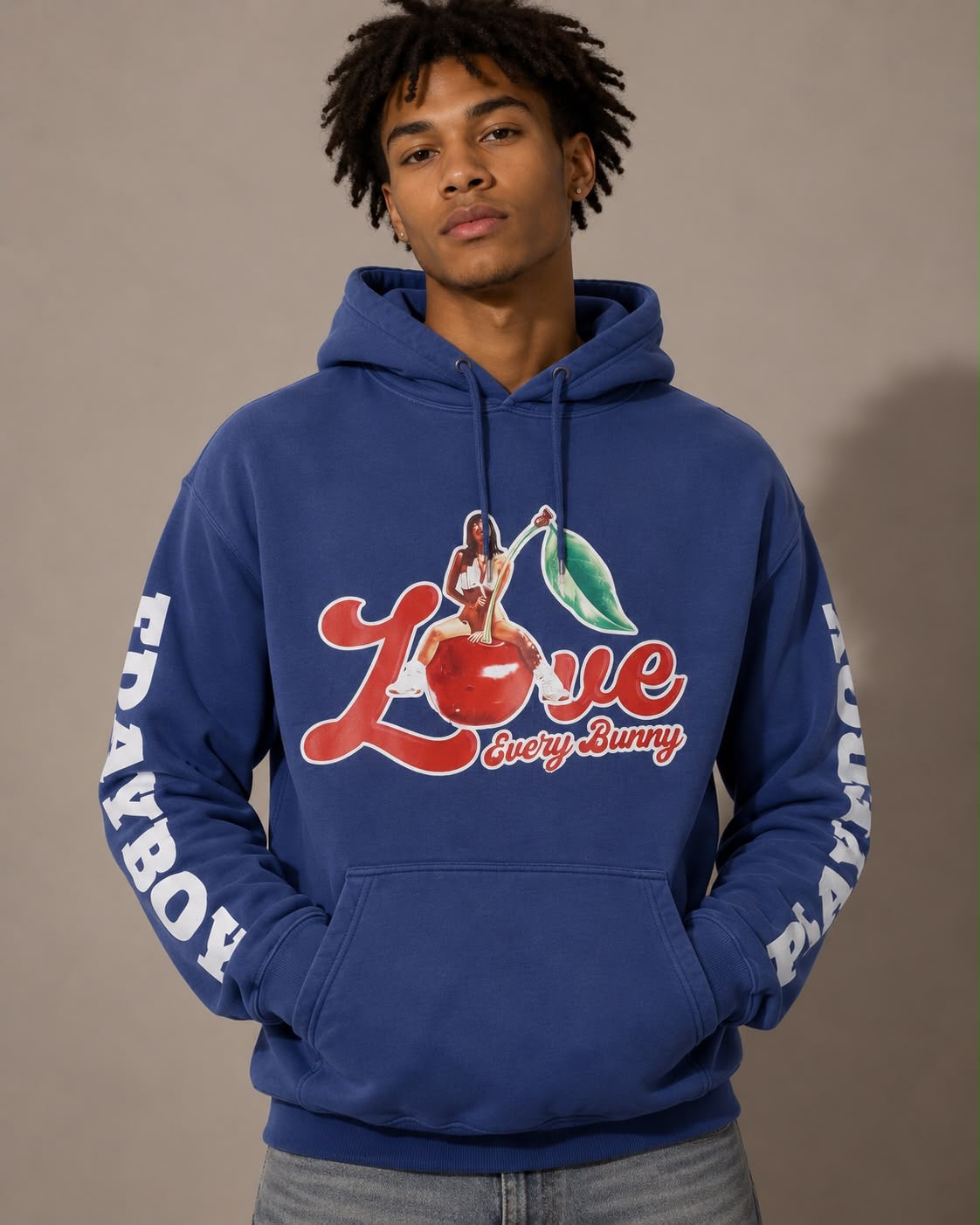 A man wearing a royal blue hoodie with a 'Love Every Bunny' graphic on the chest and 'PLAYBOY' printed down both sleeves, posed against a solid taupe background.