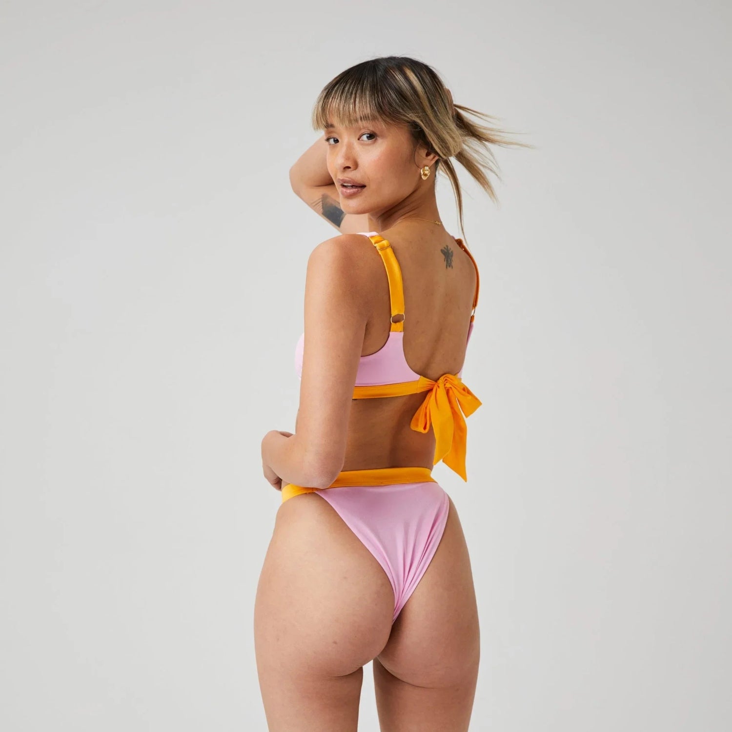 Woman modeling high-leg pink and orange bikini bottom with tie-back, viewed from behind