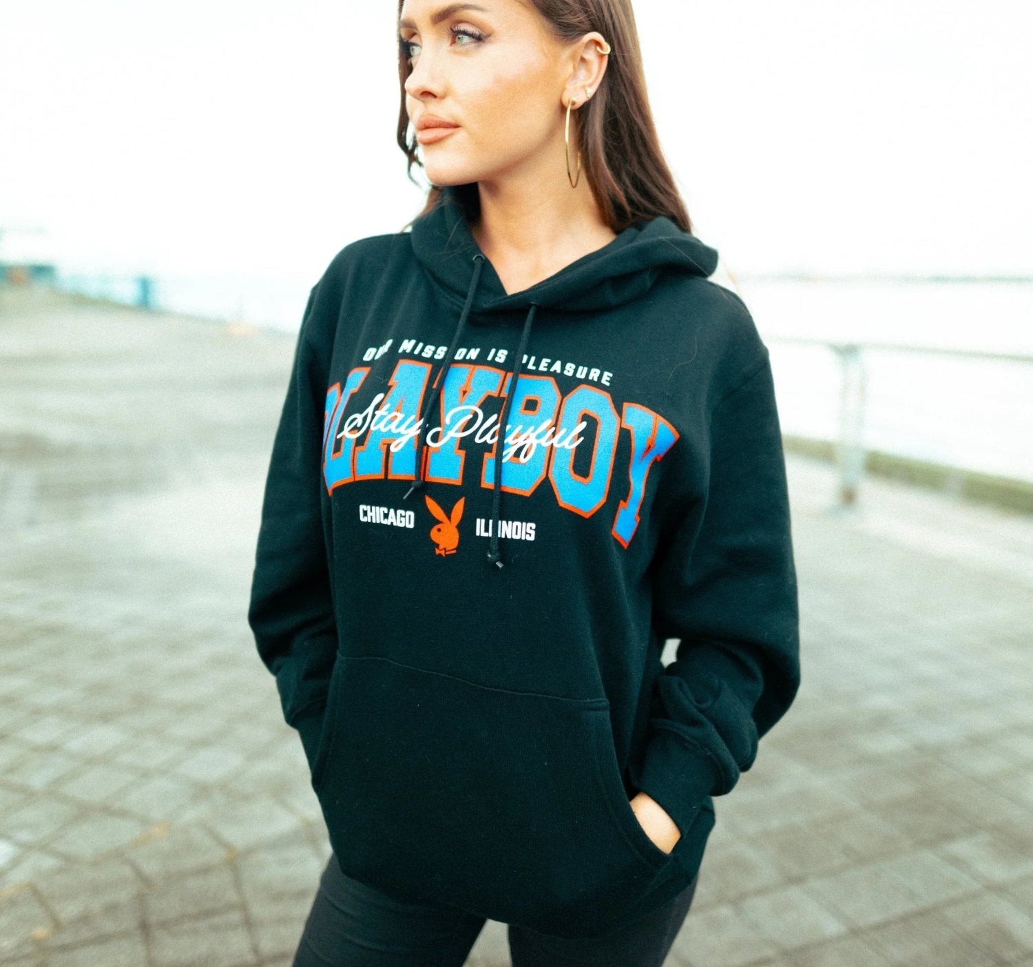 Woman wearing black graphic hoodie with colorful collegiate text and logo, outdoor setting