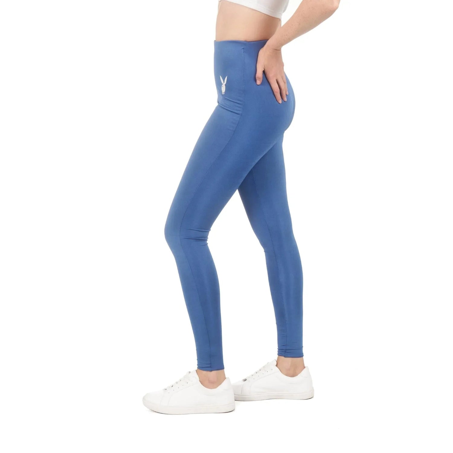 Woman in blue high-waisted leggings with white bunny logo, white crop top, and white sneakers