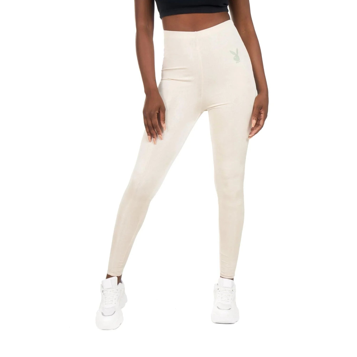 Woman wearing high-waisted beige leggings with logo, white sneakers and black crop top