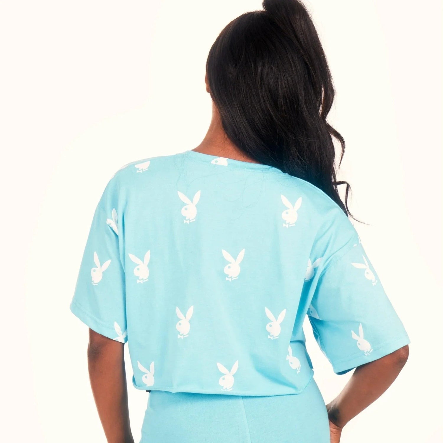 Woman wearing light blue cropped t-shirt with white bunny logo print, back view