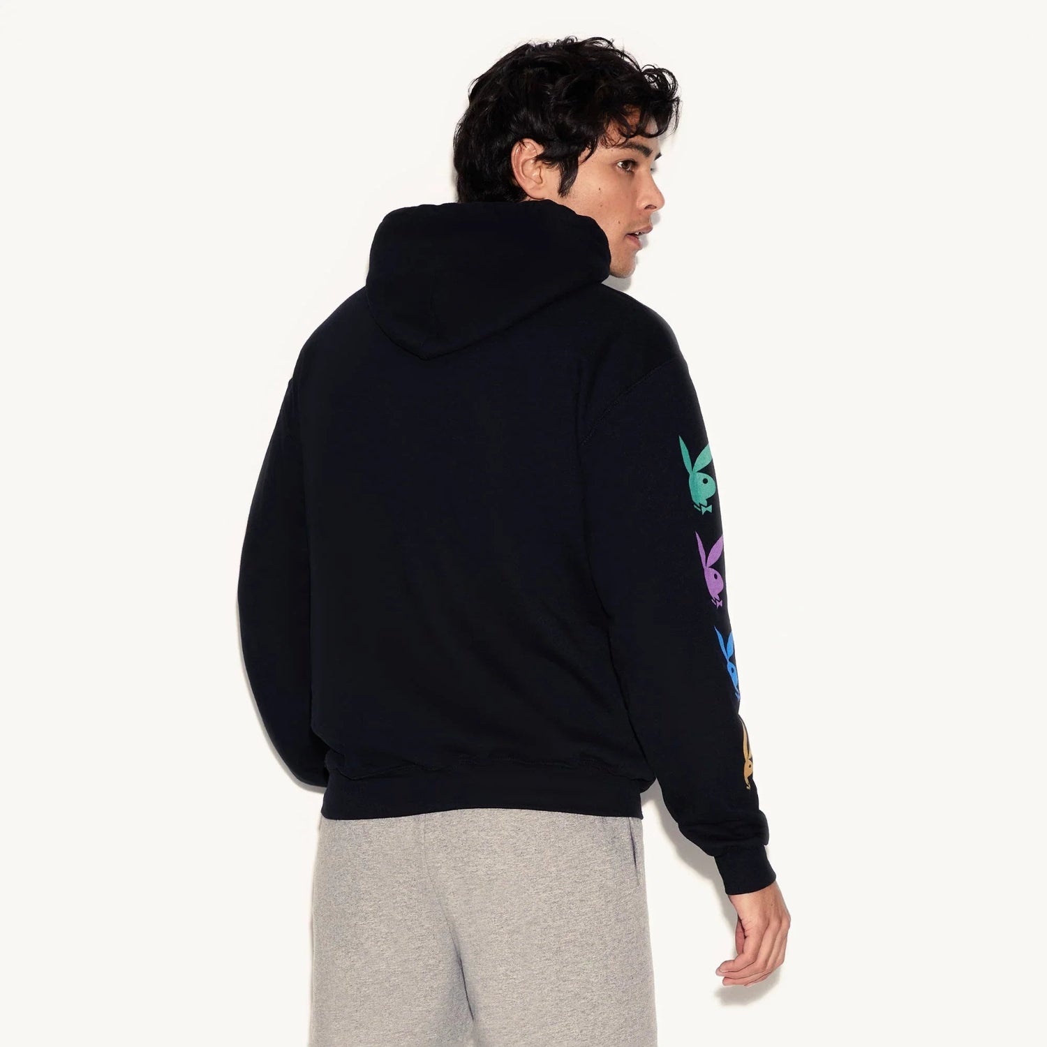 Man wearing black hoodie with colorful bunny logos on sleeve and gray sweatpants
