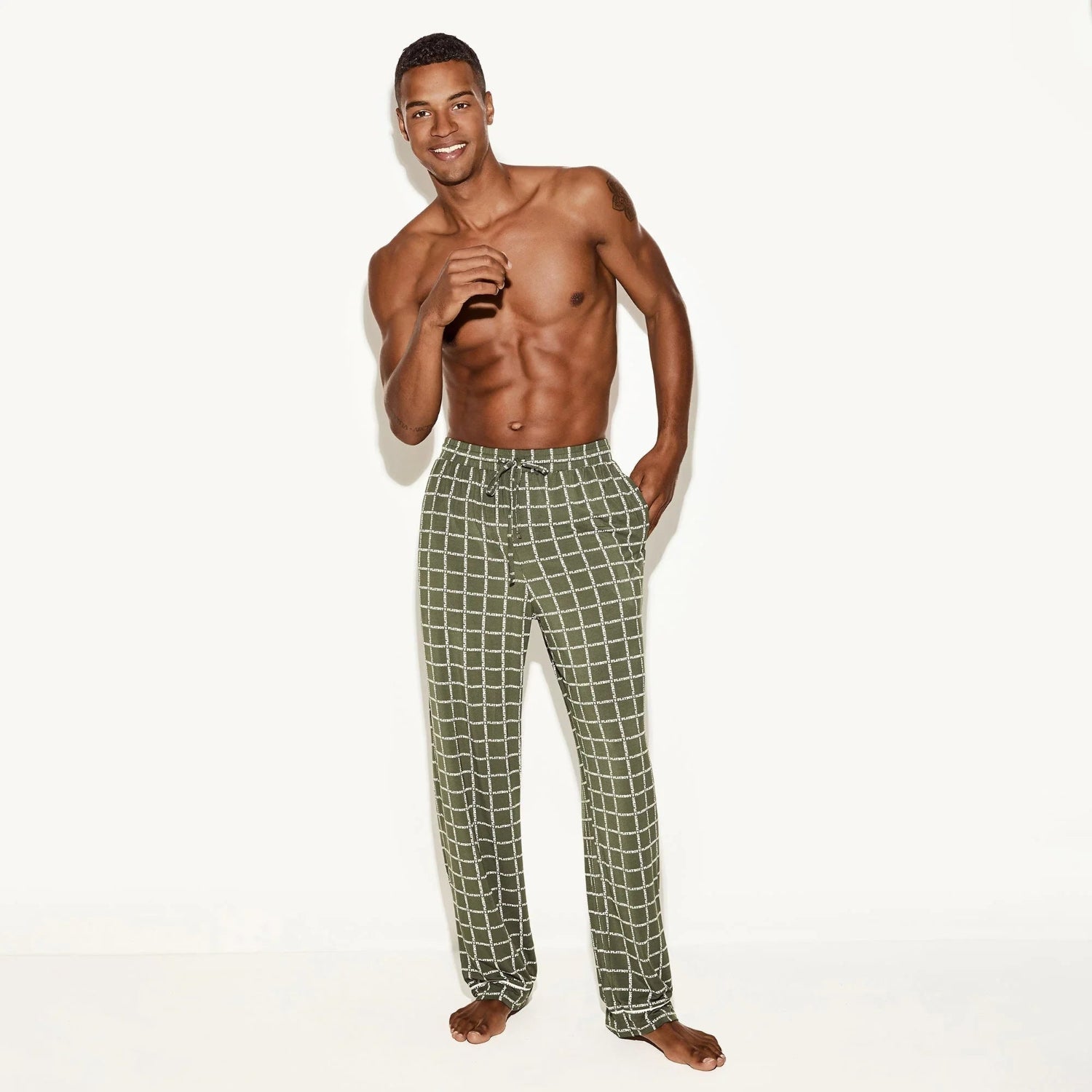 Smiling man modeling green plaid men’s sleep pants on white background