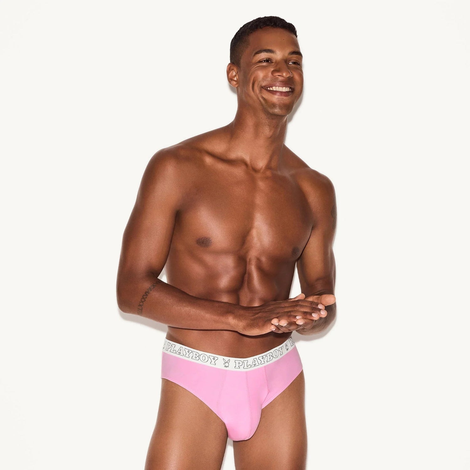 Smiling man modeling pink men's brief underwear with logo waistband on white background