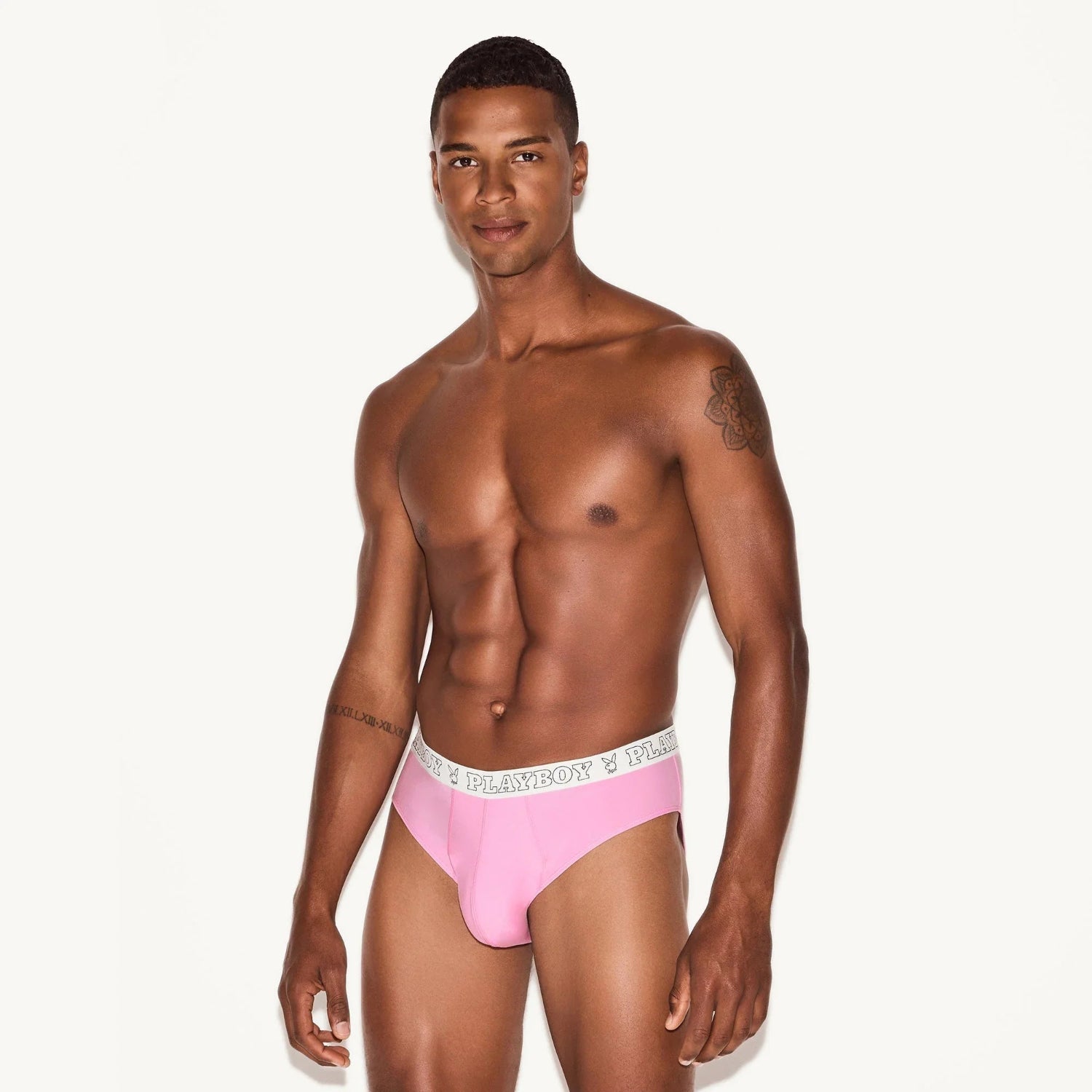 Male model wearing pink modal brief underwear with white logo waistband, standing against light background.