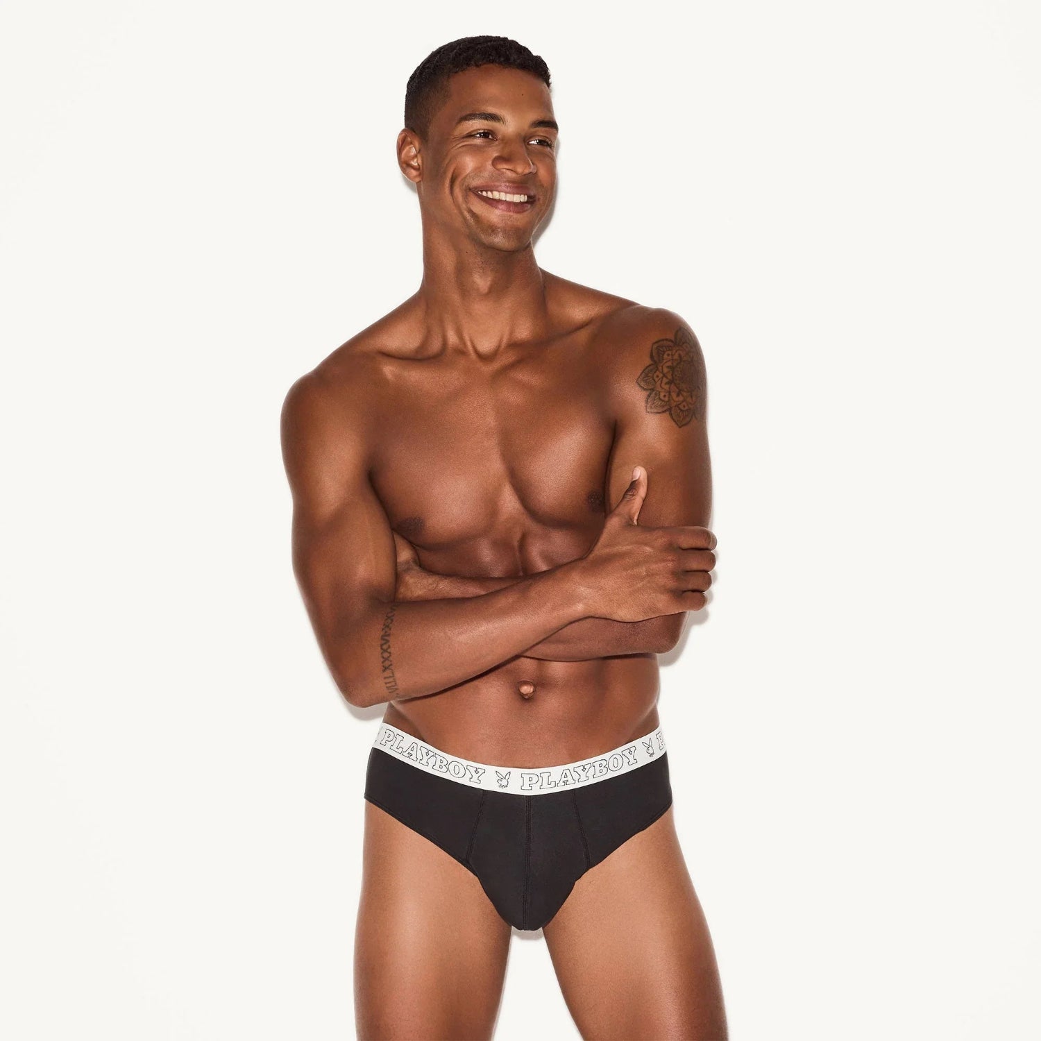 Smiling man modeling black modal men's briefs with a white waistband and logo, studio background.