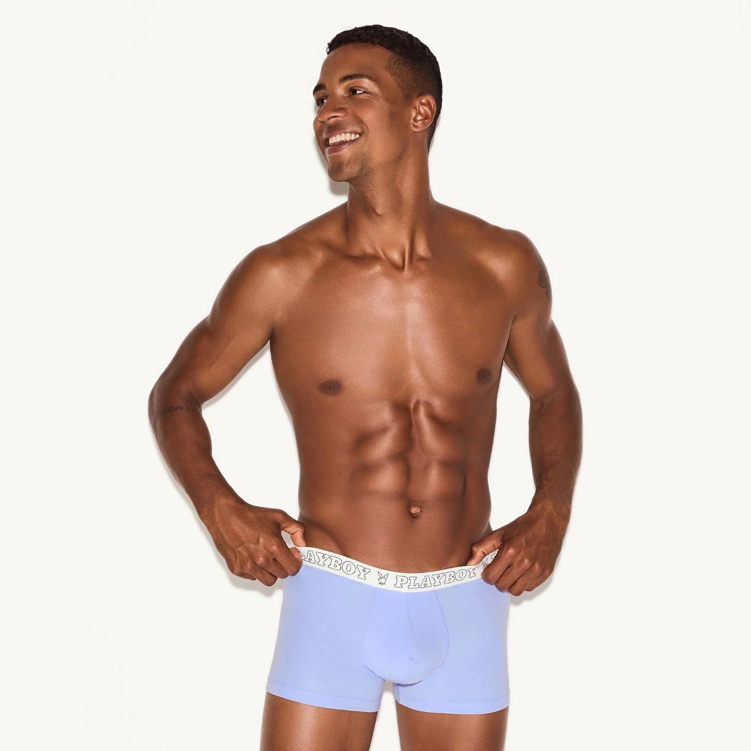 Smiling man modeling light blue men's modal trunk underwear with logo waistband.