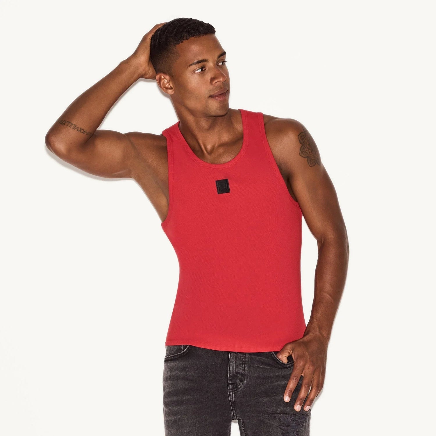 Man wearing red ribbed tank top and black jeans posing on white background