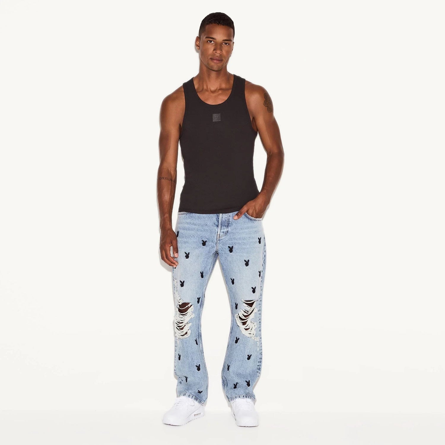Man wearing black ribbed tank top and light blue ripped jeans with black bunny print