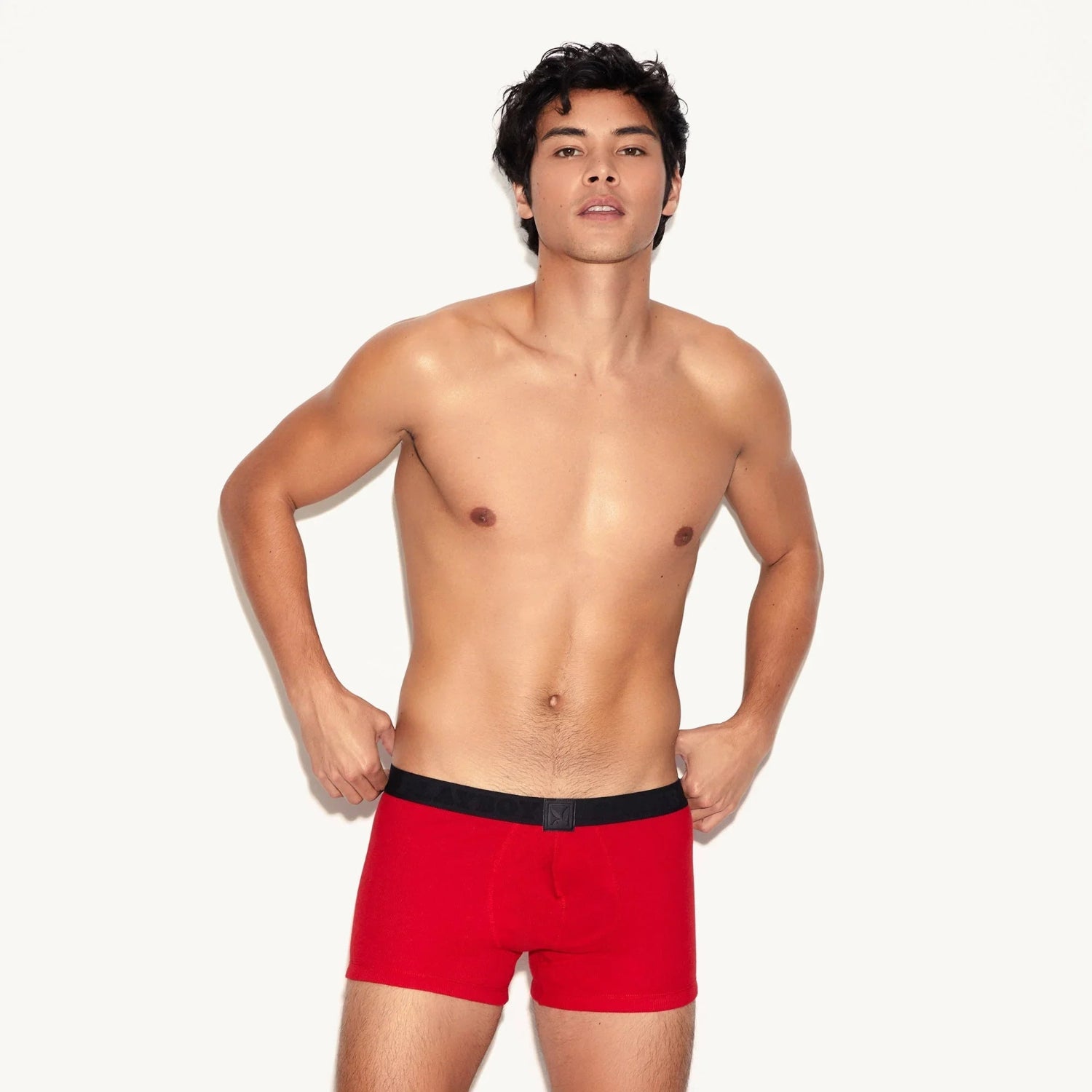 Shirtless male model wearing red ribbed men's trunks with black waistband, neutral background.