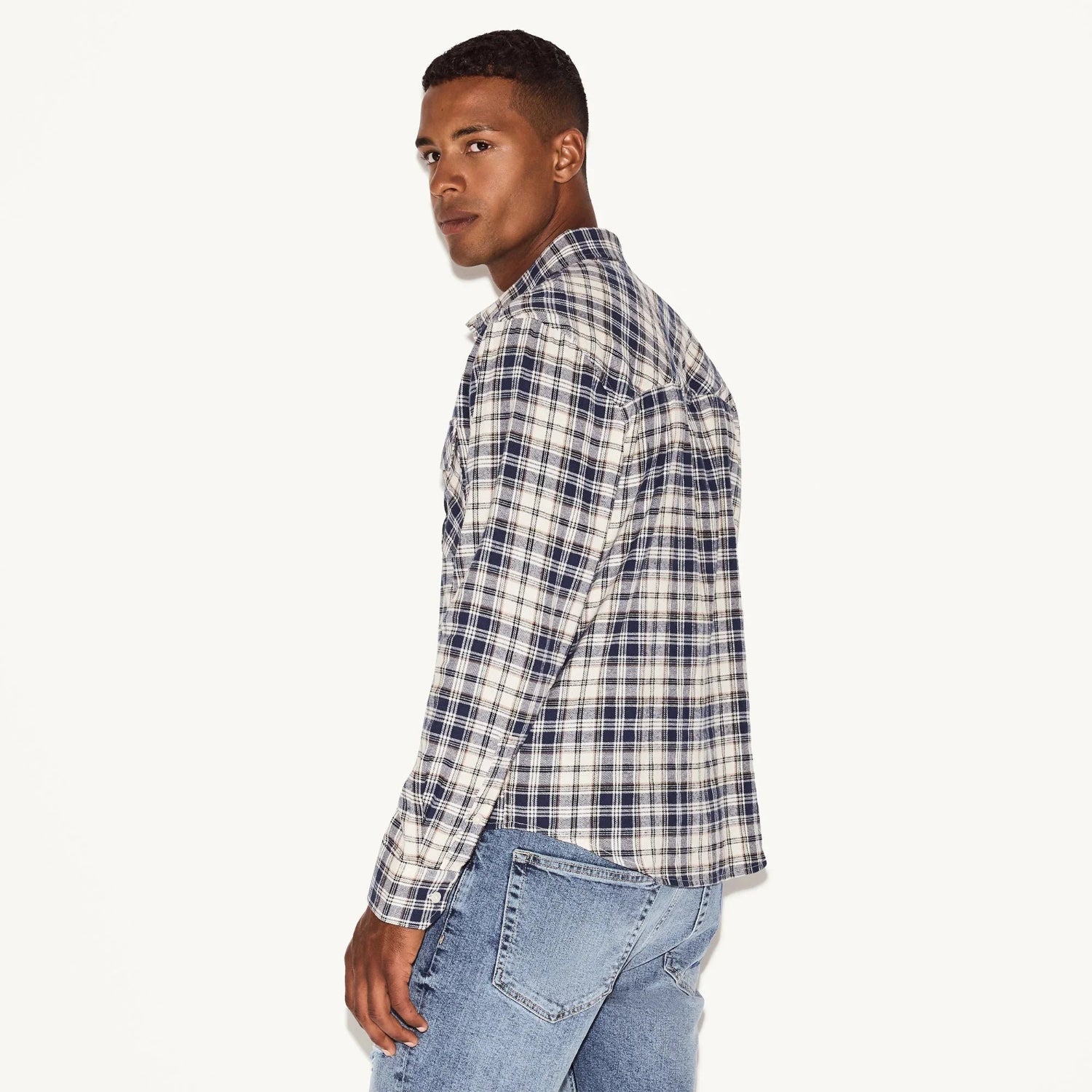 Man wearing blue plaid flannel long sleeve shirt and light denim jeans, turned sideways