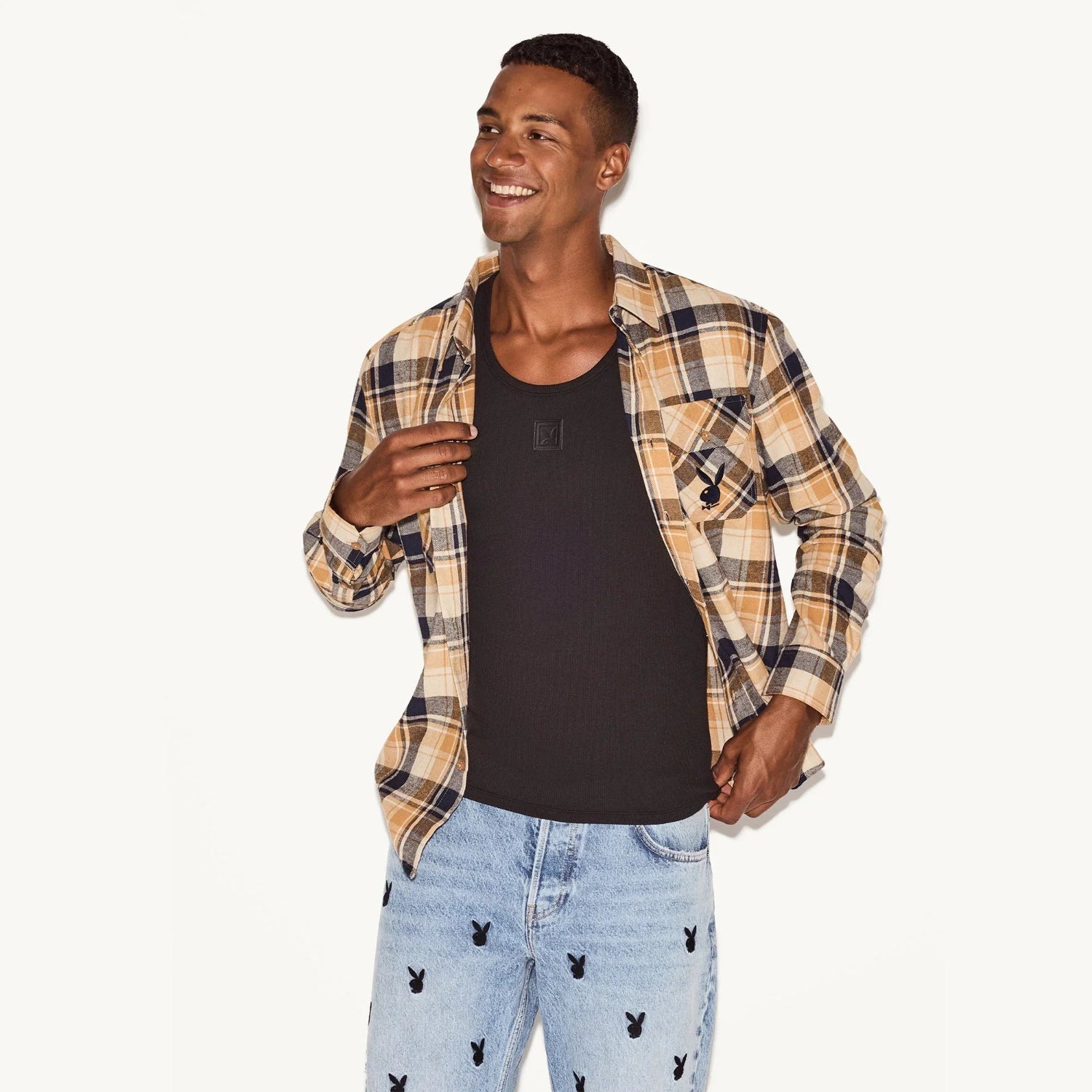 Man wearing beige plaid flannel shirt and light blue jeans with black bunny logos
