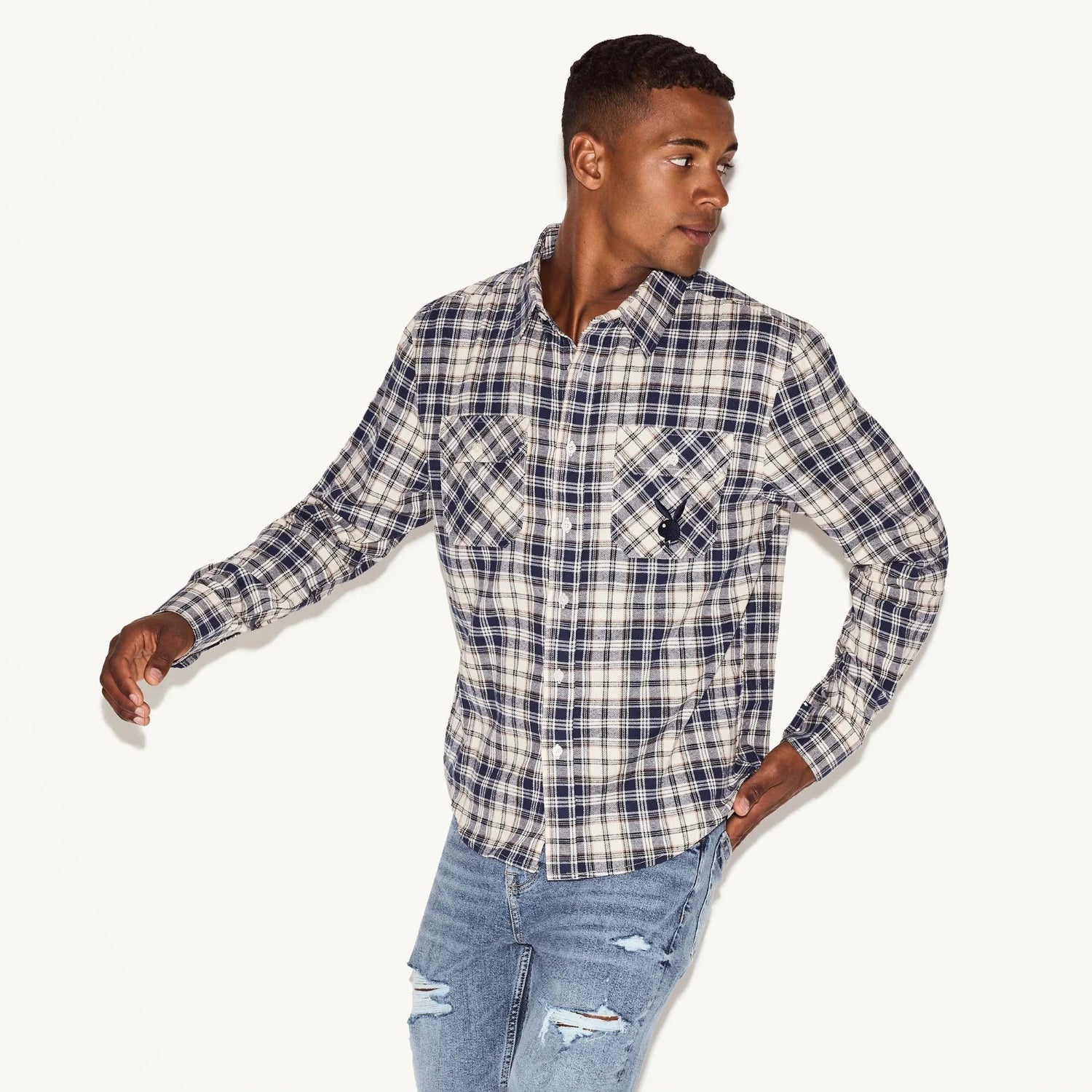 Man wearing a blue plaid flannel long sleeve shirt and ripped jeans on white background
