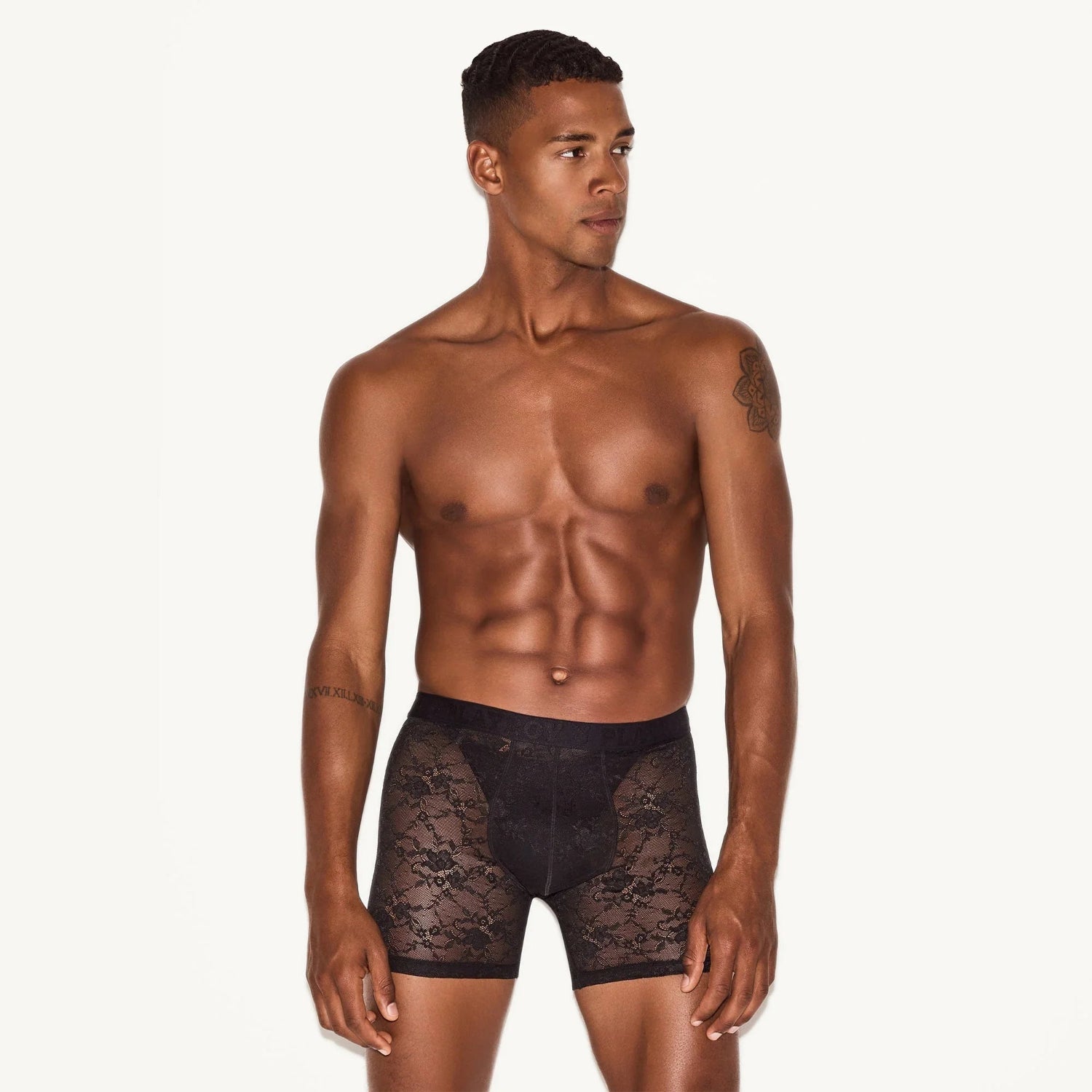 Male model wearing black lace boxer briefs against light background