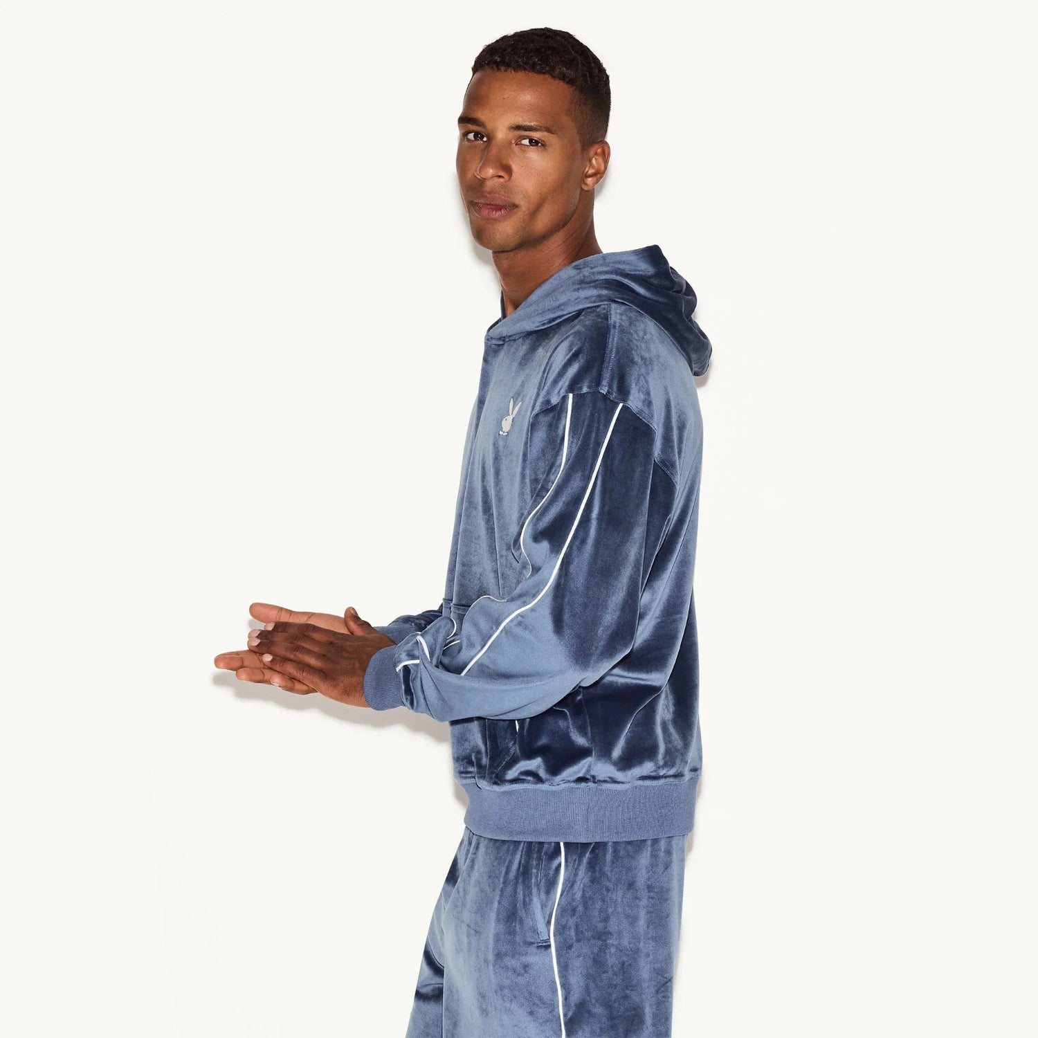 Man wearing blue velour hoodie and matching joggers with white piping detail