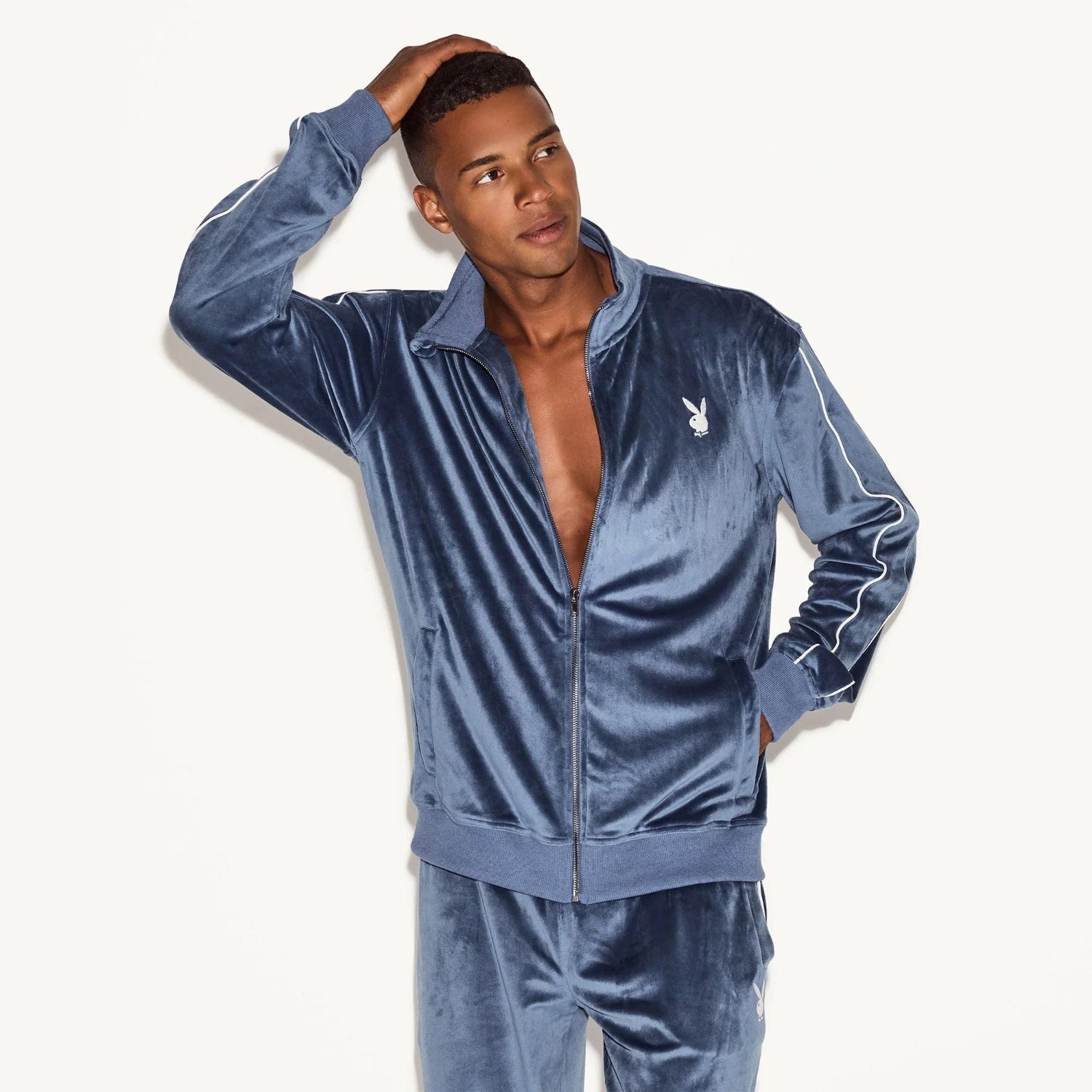 Man wearing a blue velour track jacket with white logo and matching pants, standing indoors.