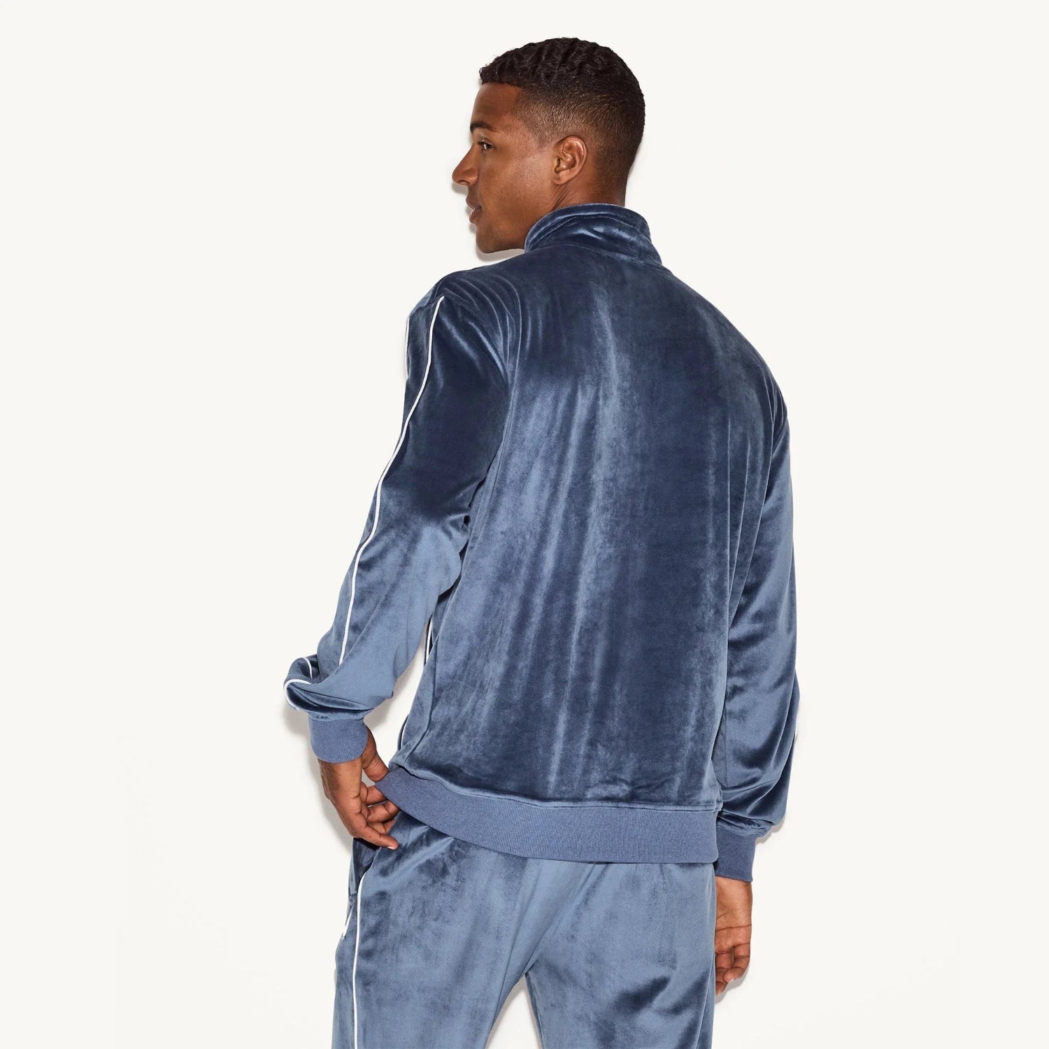 Man wearing blue velour track jacket and pants with white piping, back view