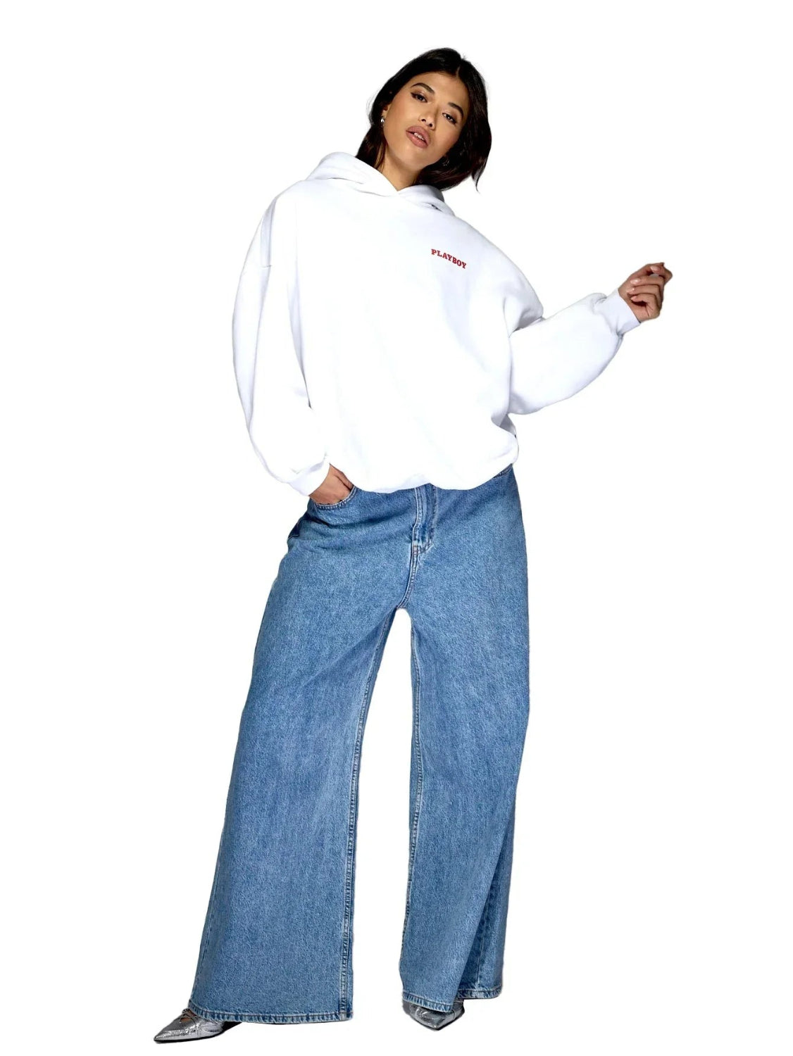 Woman wearing white hooded sweatshirt with red text and wide-leg blue jeans