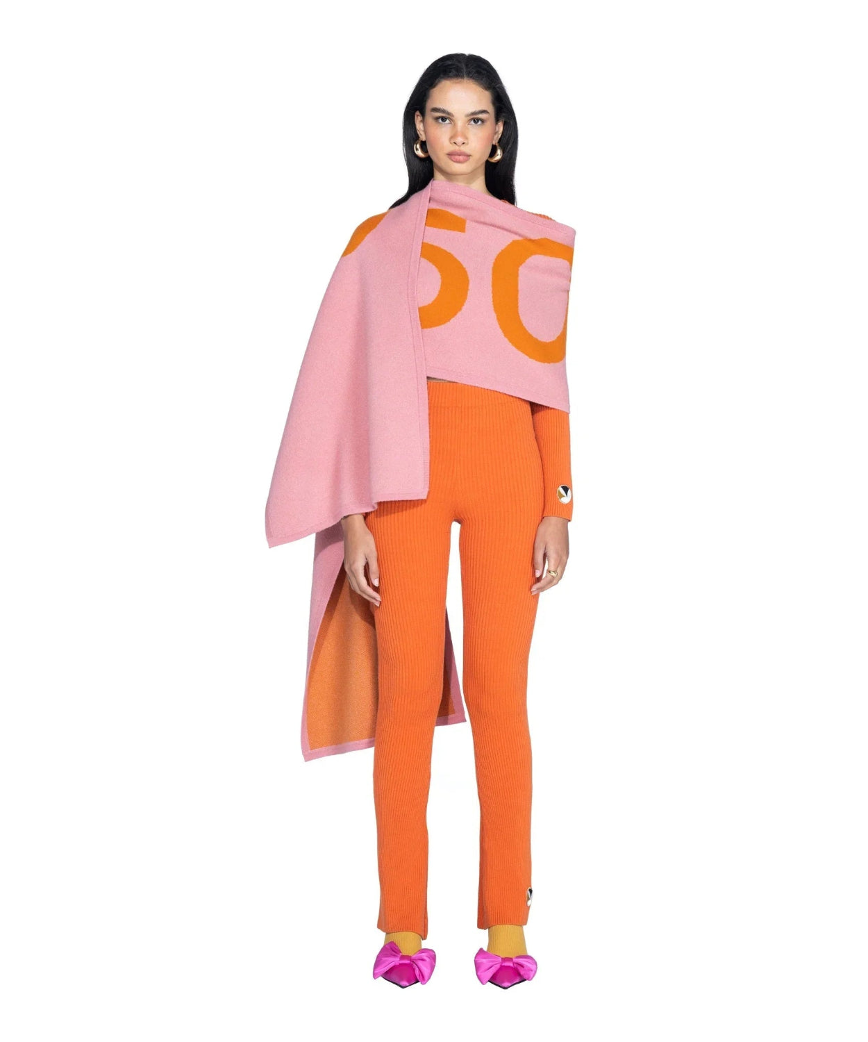 Woman wearing pink and orange cashmere scarf, orange ribbed sweater pants, and pink bow shoes
