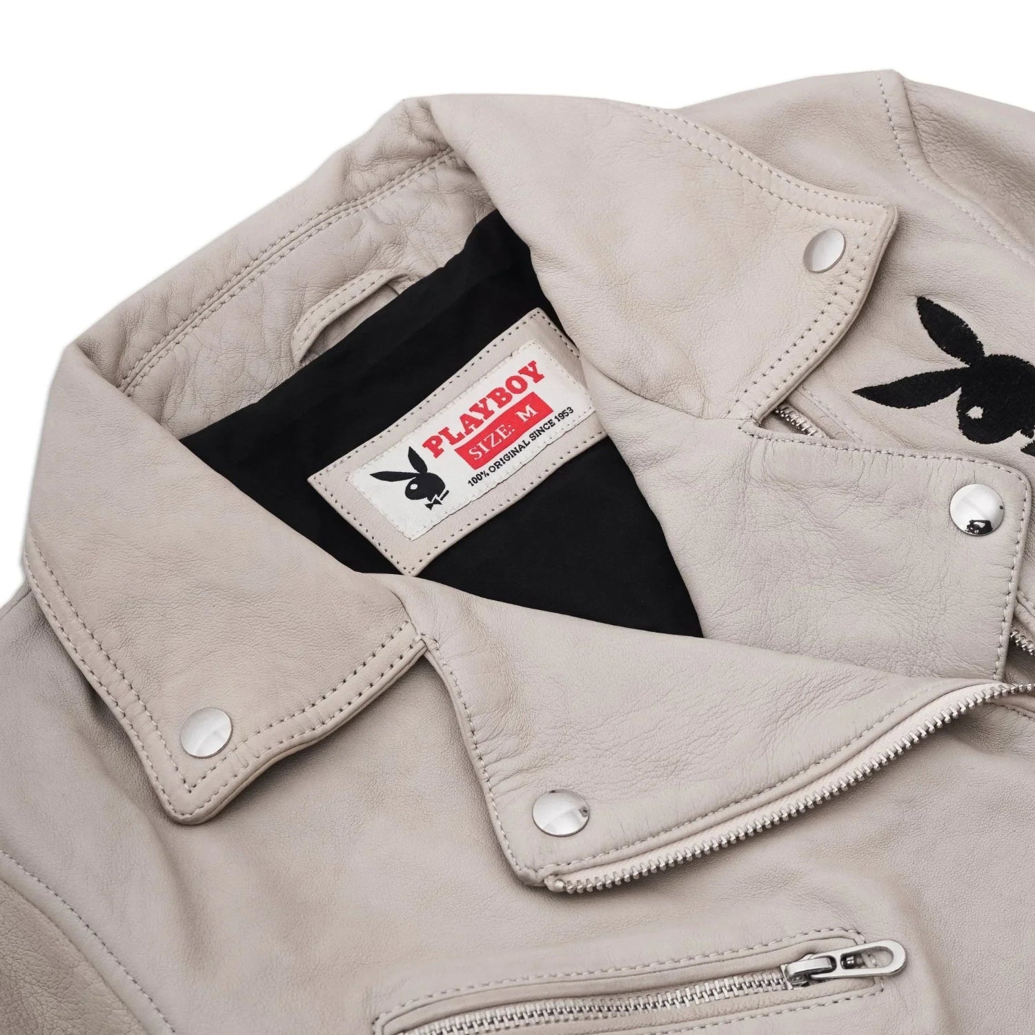 Women's beige leather jacket with metal snaps, zippers, and visible rabbit head patch on chest