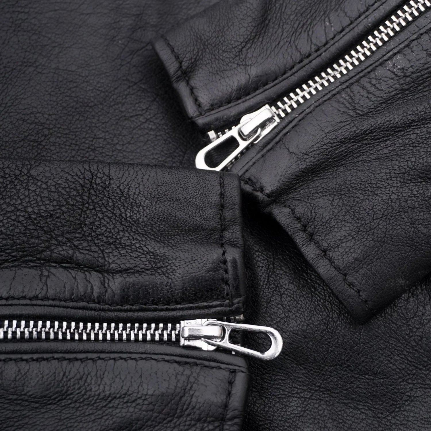 Close-up of black women's leather jacket sleeves with silver zippers and textured finish