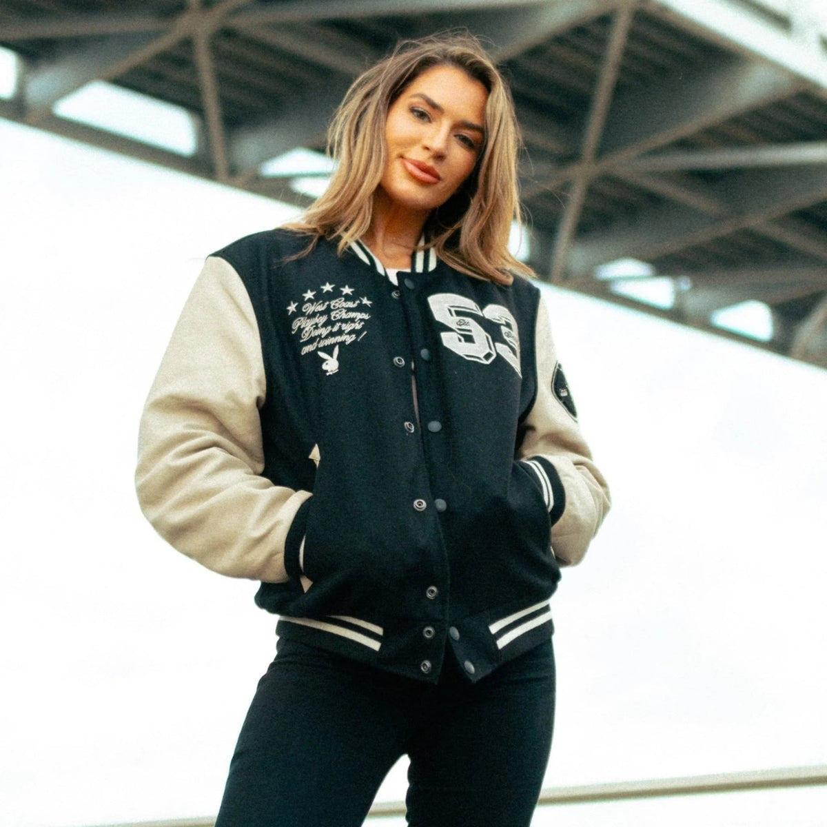 Woman wearing a black and beige varsity jacket with embroidered patches and striped cuffs