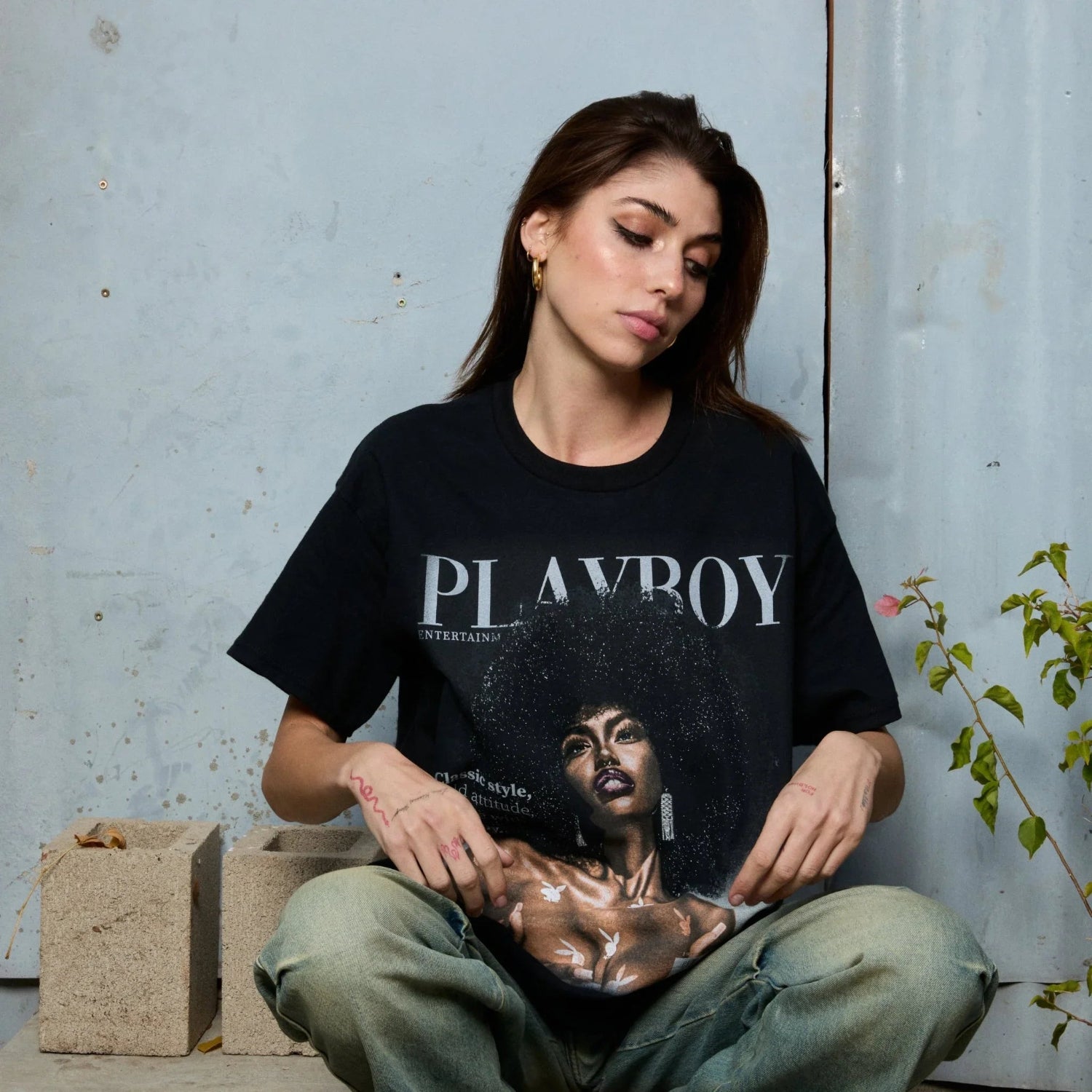Woman wearing black graphic Playboy T-shirt with model print, sitting casually outdoors