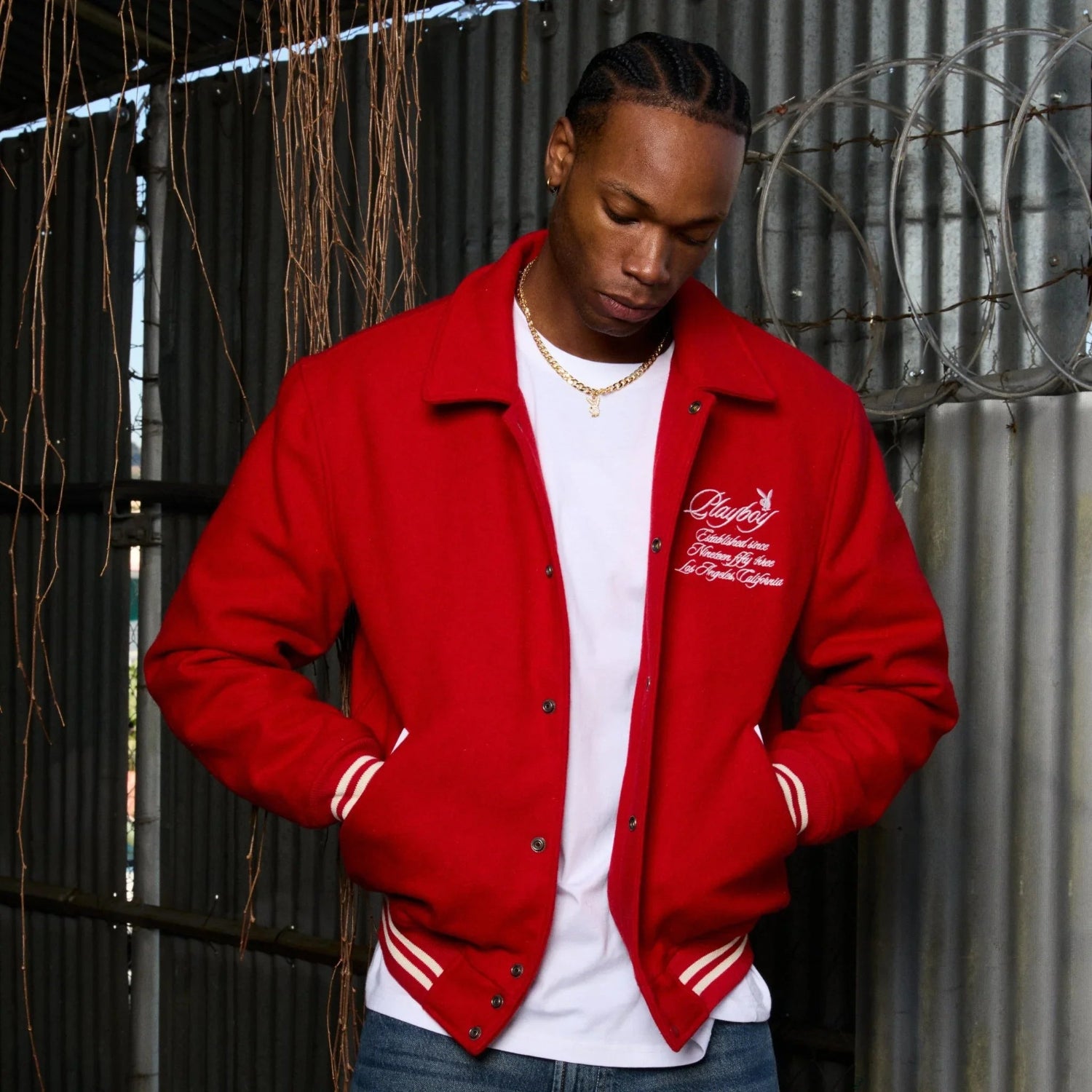 Man wearing a red varsity jacket with white embroidered text and striped cuffs, casual style