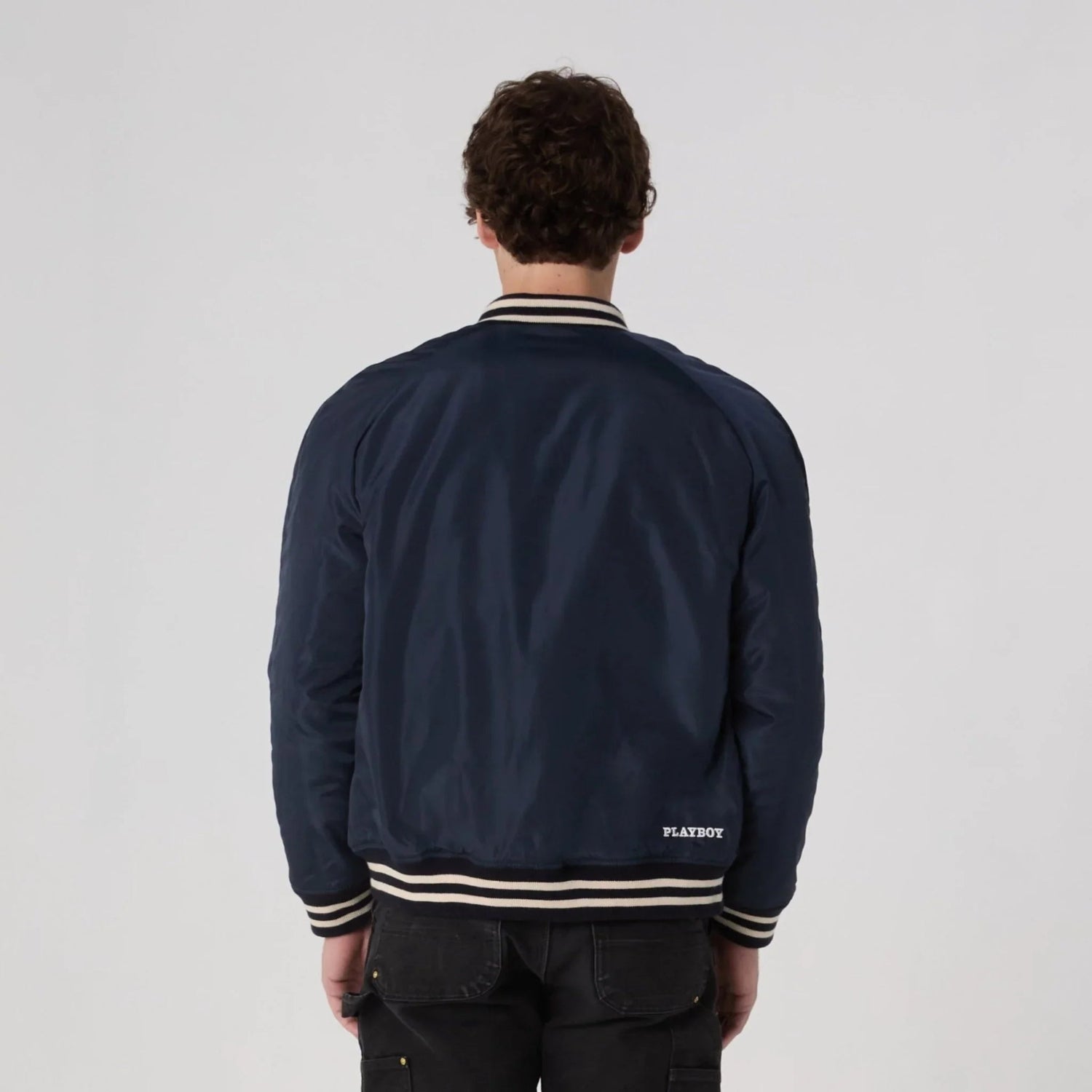 Man wearing navy varsity jacket with striped collar and PLAYBOY text on lower back