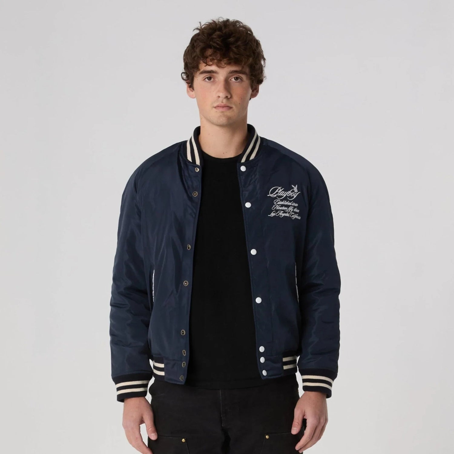 Man wearing navy blue varsity jacket with white script embroidery and striped trim