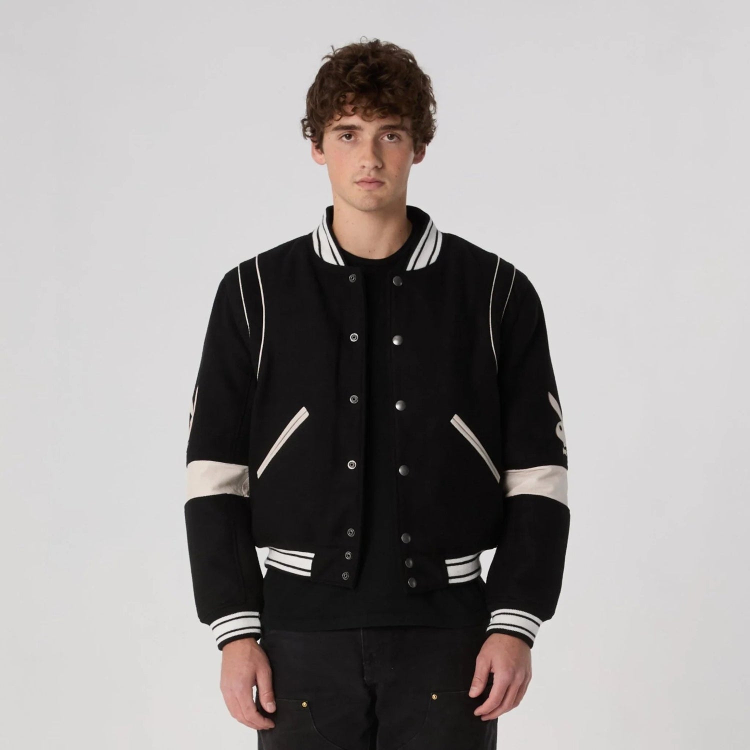 Man wearing black and white varsity jacket with snap buttons and striped trim