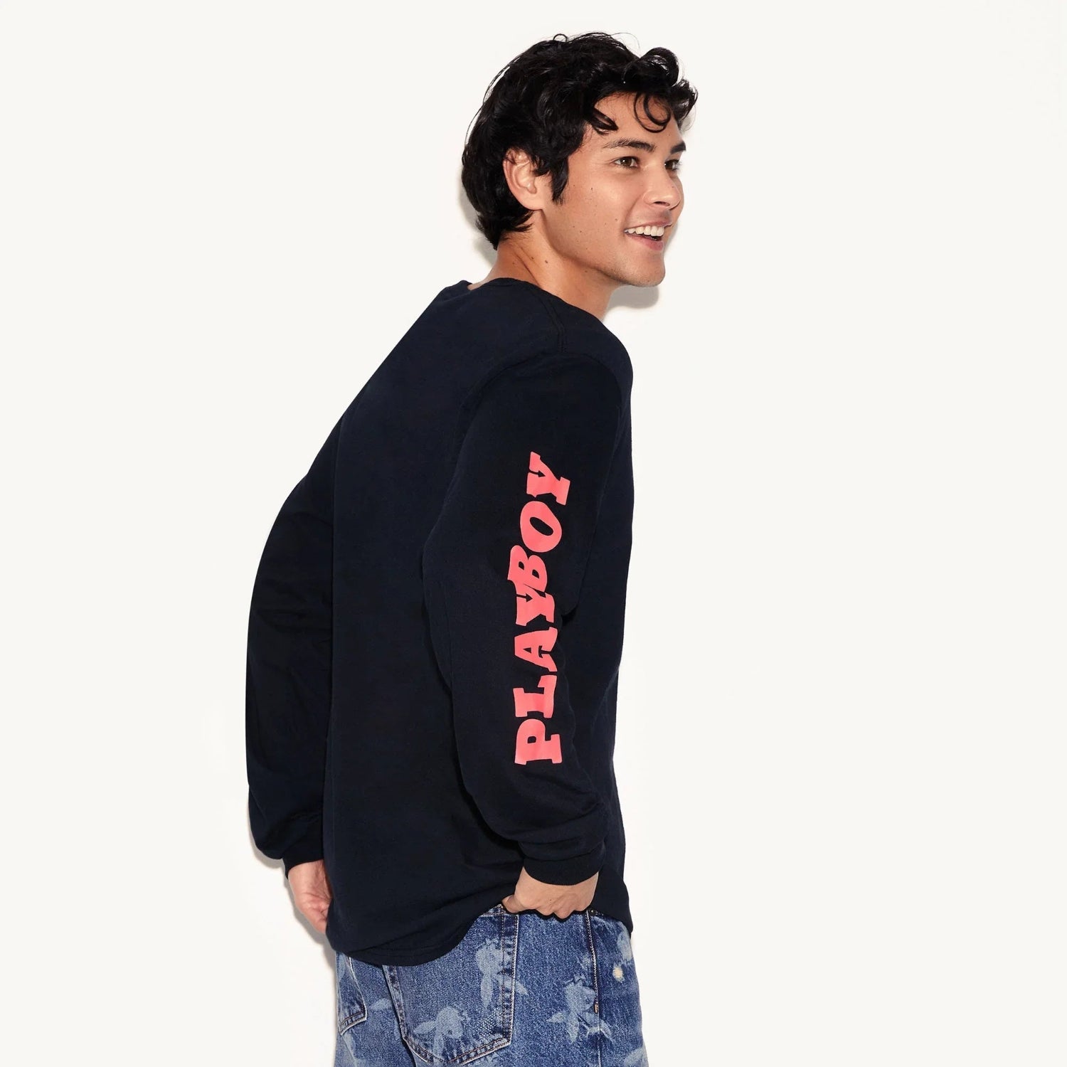 Man wearing black long sleeve t-shirt with pink PLAYBOY text on sleeve, casual jeans