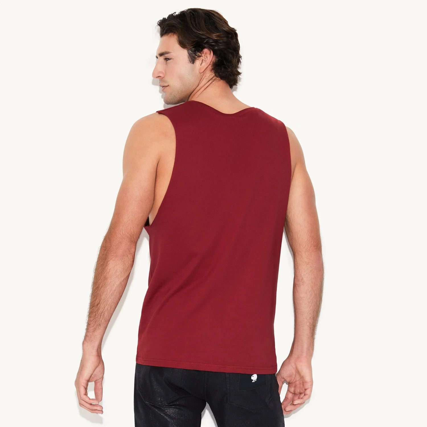 Man wearing a sleeveless maroon muscle tank top, shown from the back, paired with black jeans.
