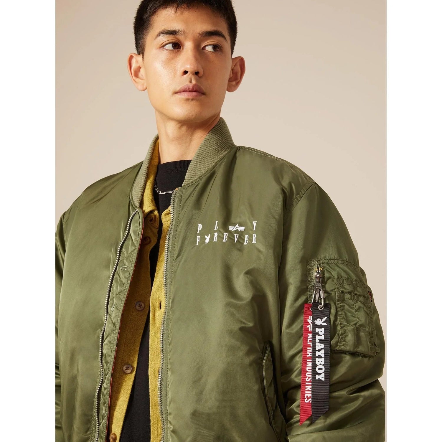 Man wearing olive green reversible MA-1 flight jacket with PLAY FOREVER text and branded tags