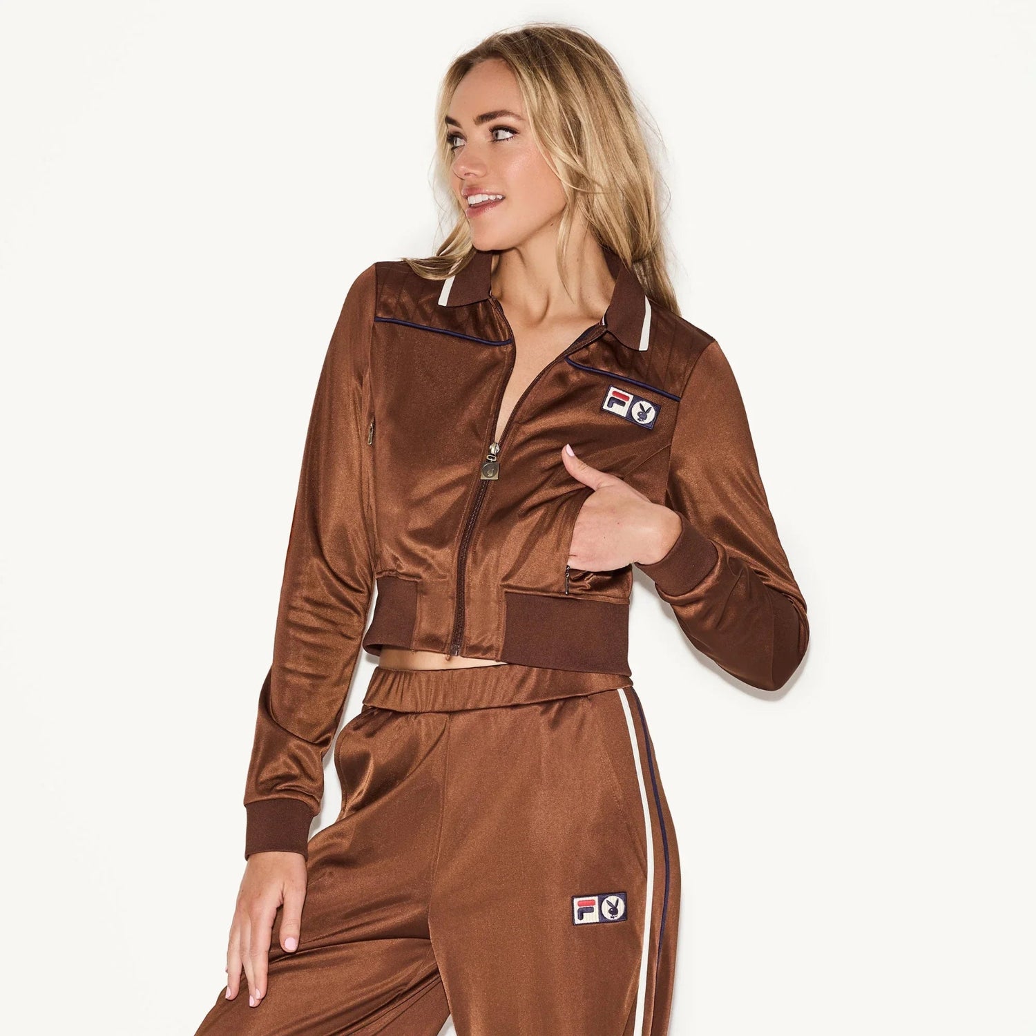 Woman wearing brown slim fit zip-up track jacket and matching pants with logo patches.