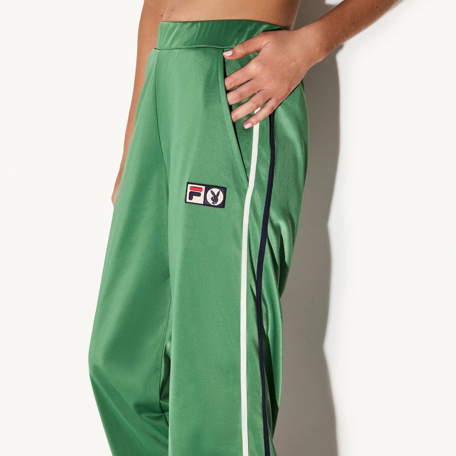 Green track pants with side stripes and front Fila and rabbit logo patch, close-up view