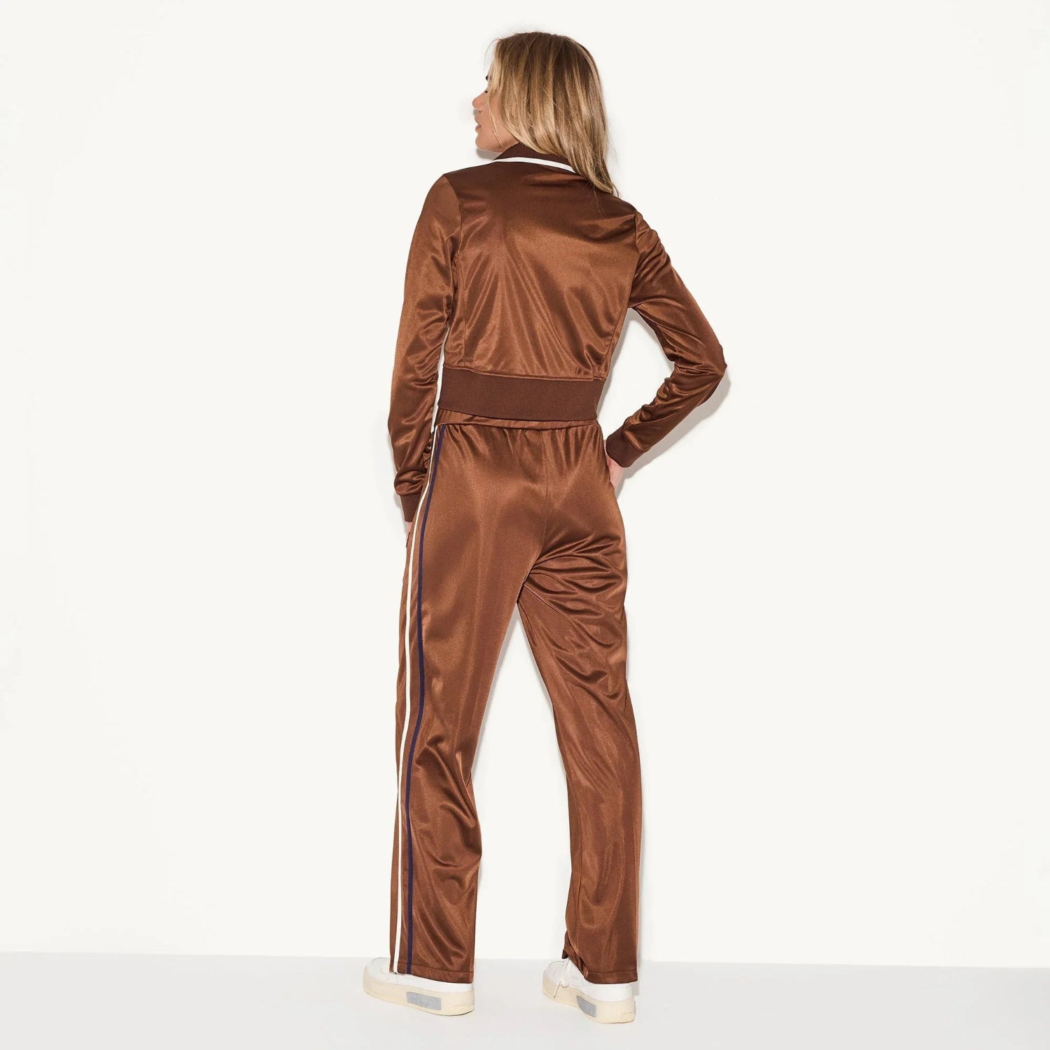 Woman wearing brown satin track pants with side stripes, shown from the back