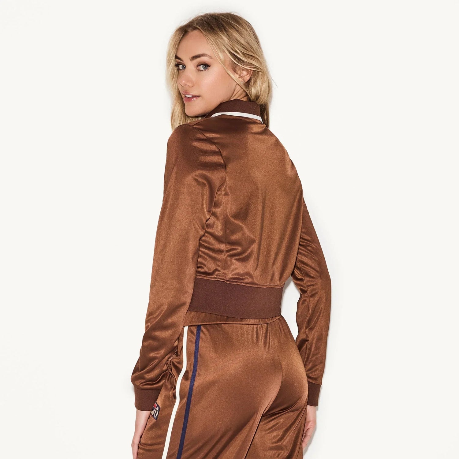 Woman wearing brown satin track jacket and matching pants with side stripes, viewed from back