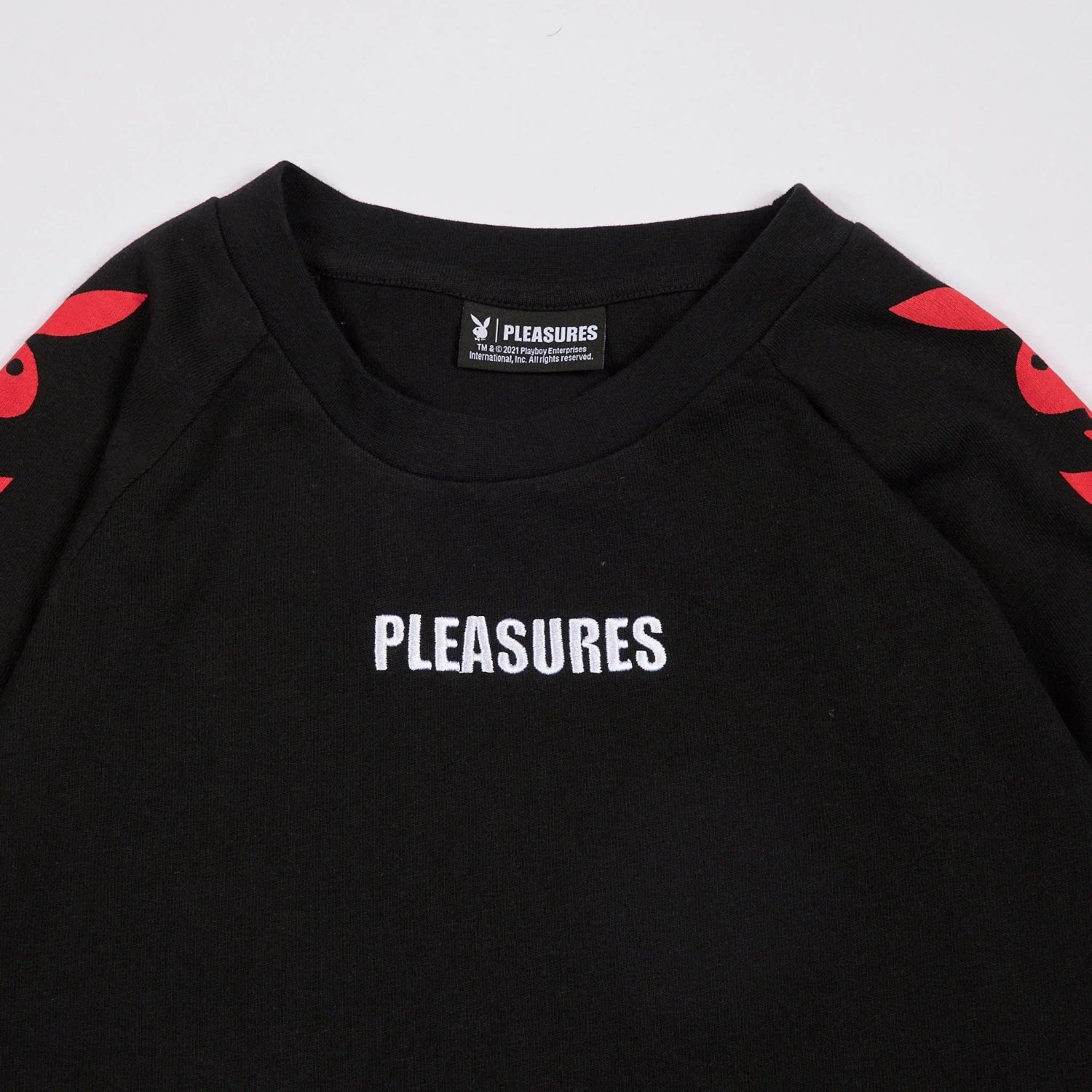 Black long sleeve raglan t-shirt with white 'PLEASURES' text and red rabbit head graphics on sleeves