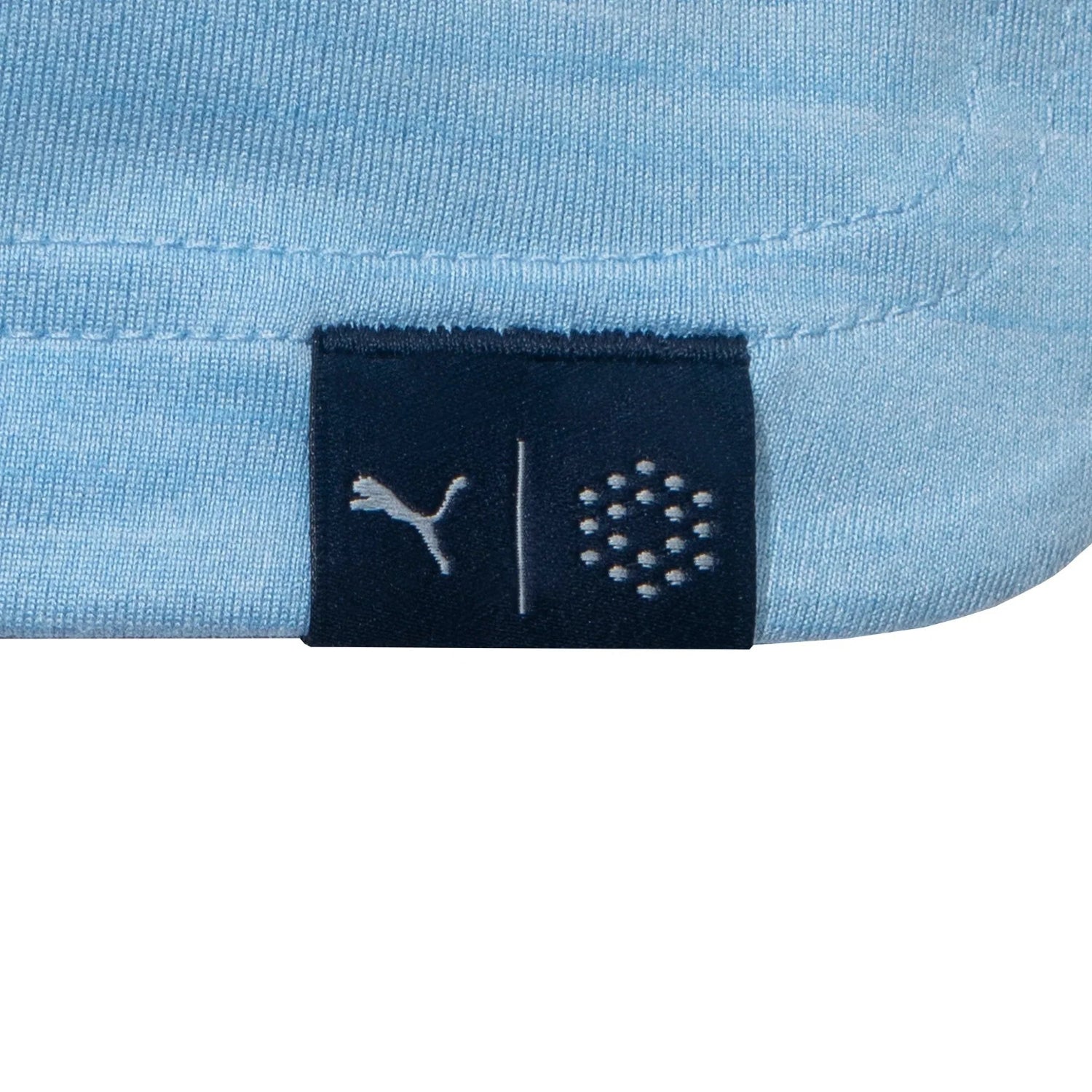 Close-up of light blue golf polo shirt hem with small navy tag and embroidered logos
