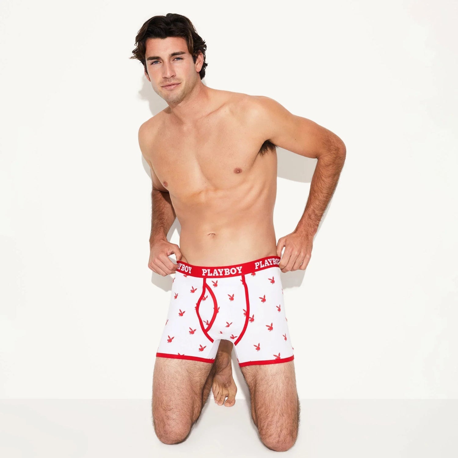 Man modeling white boxer briefs with red trim and all-over bunny head print, kneeling on floor