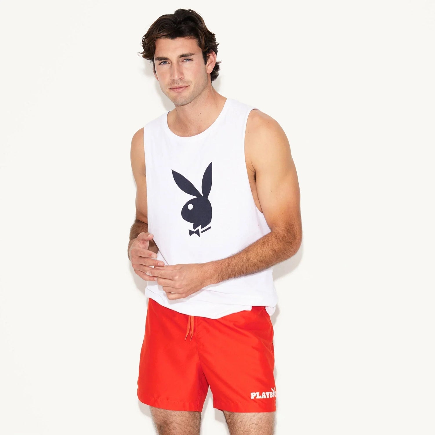 Man modeling white muscle tank with black rabbit head graphic, paired with red shorts