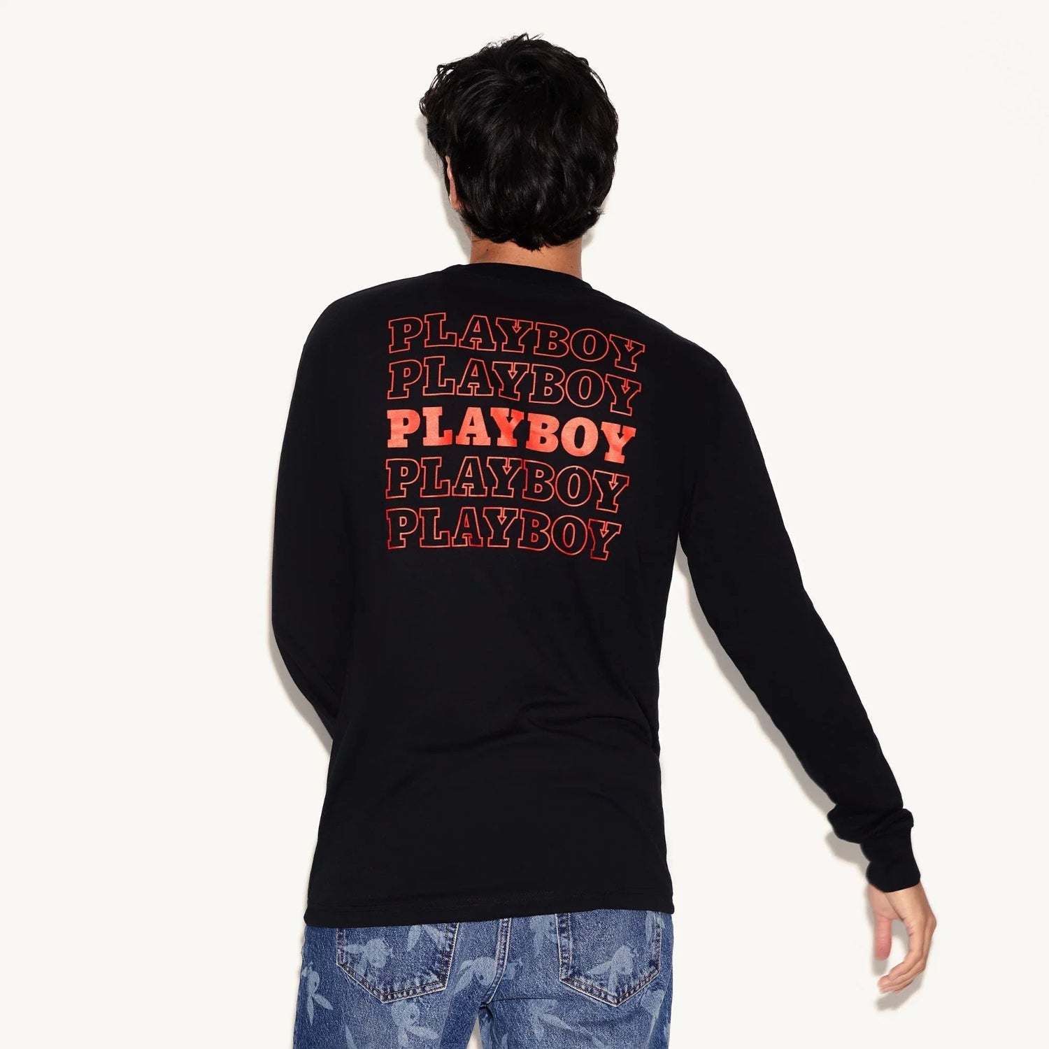 Man wearing black long sleeve t-shirt with repeating red text graphic on back, blue jeans